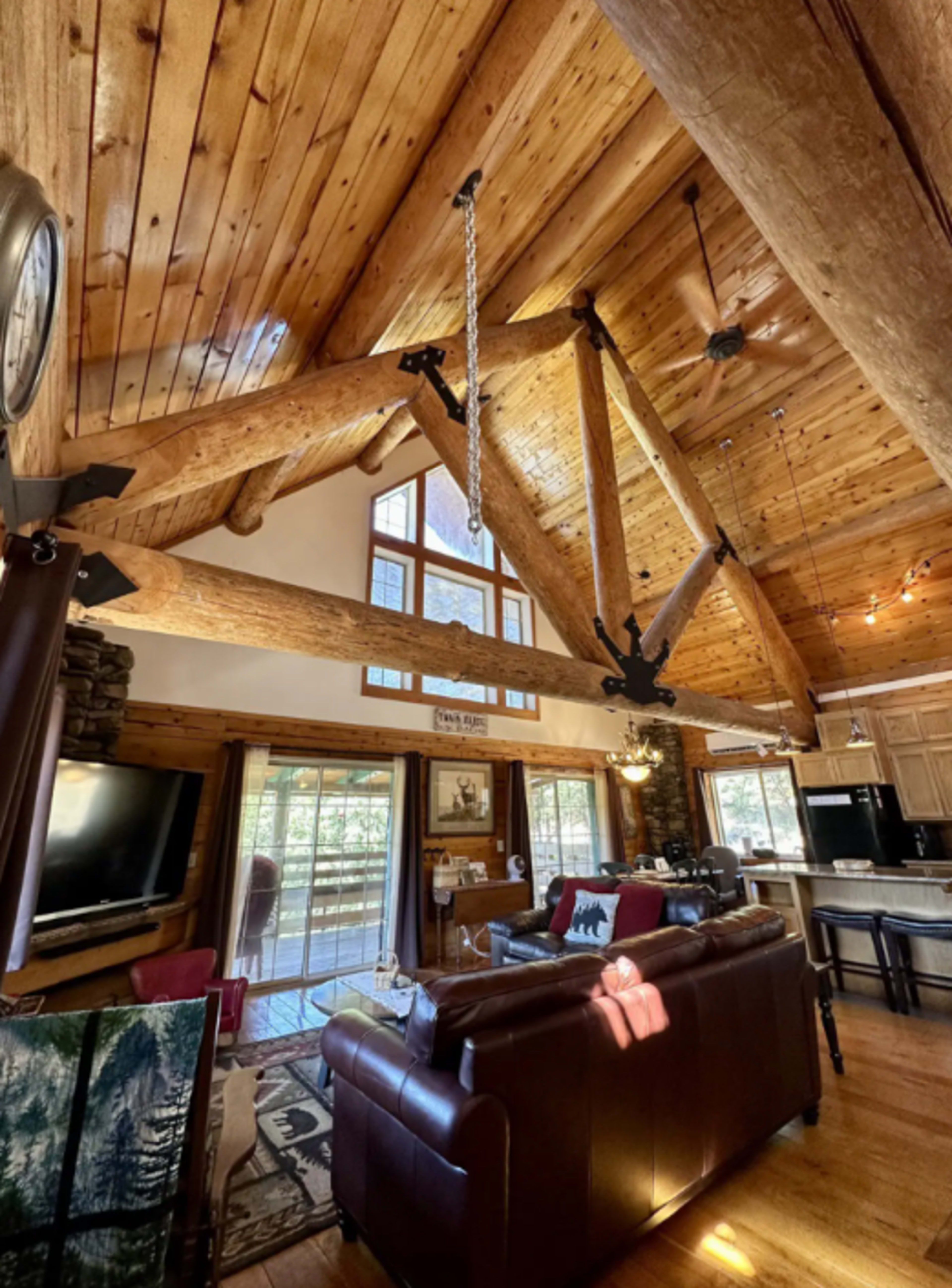 A spacious rustic living room with wooden beams, large windows, and a brown leather sofa.