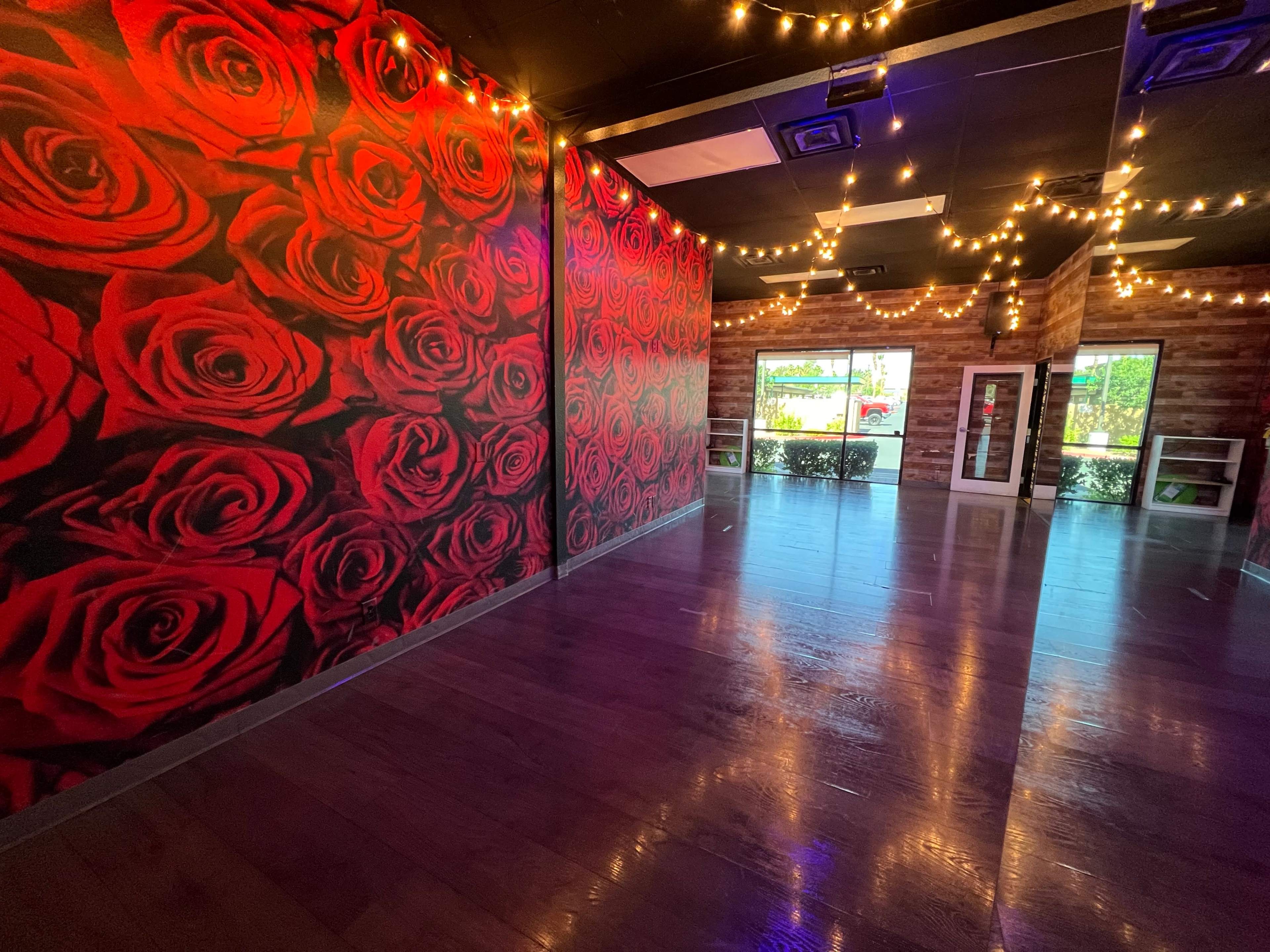 A spacious interior with a wall covered in red rose graphics and warm string lights overhead.
