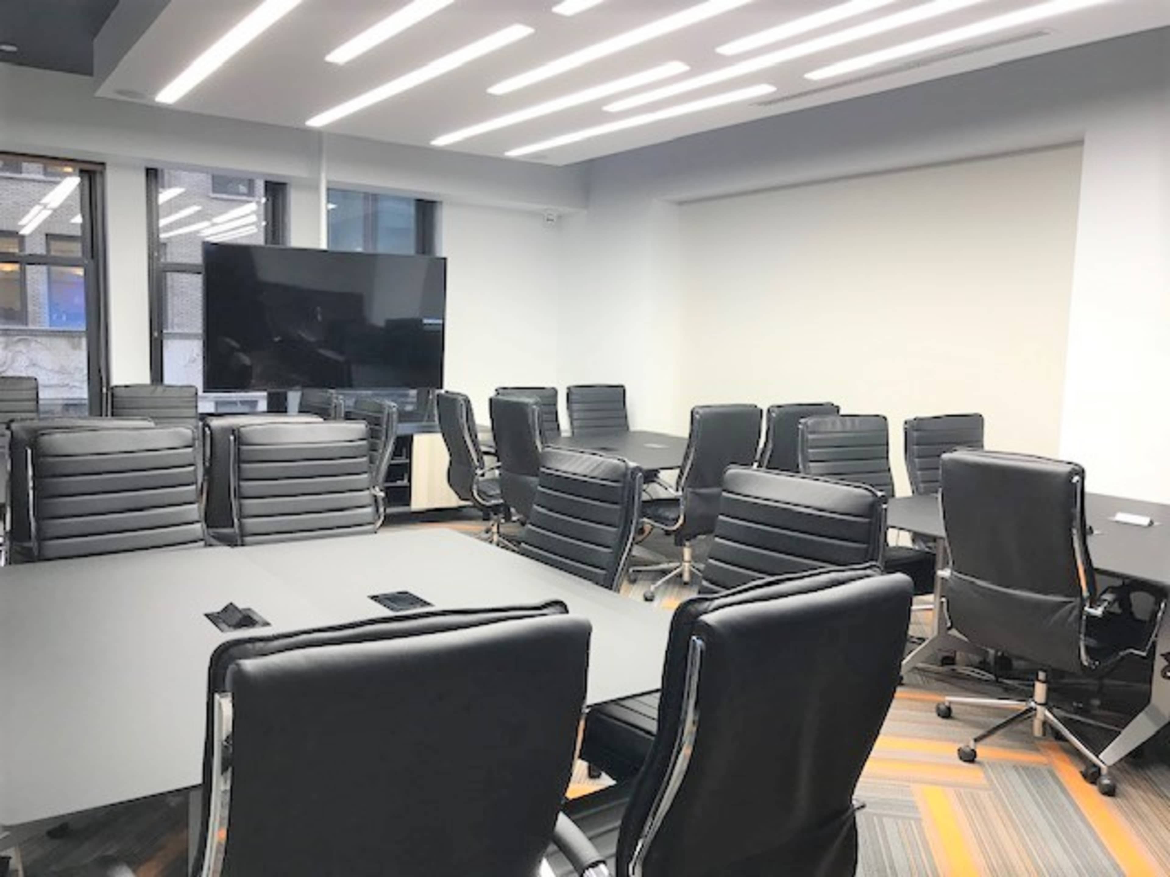 A modern conference room features a large table surrounded by several black leather chairs and a wall-mounted television.