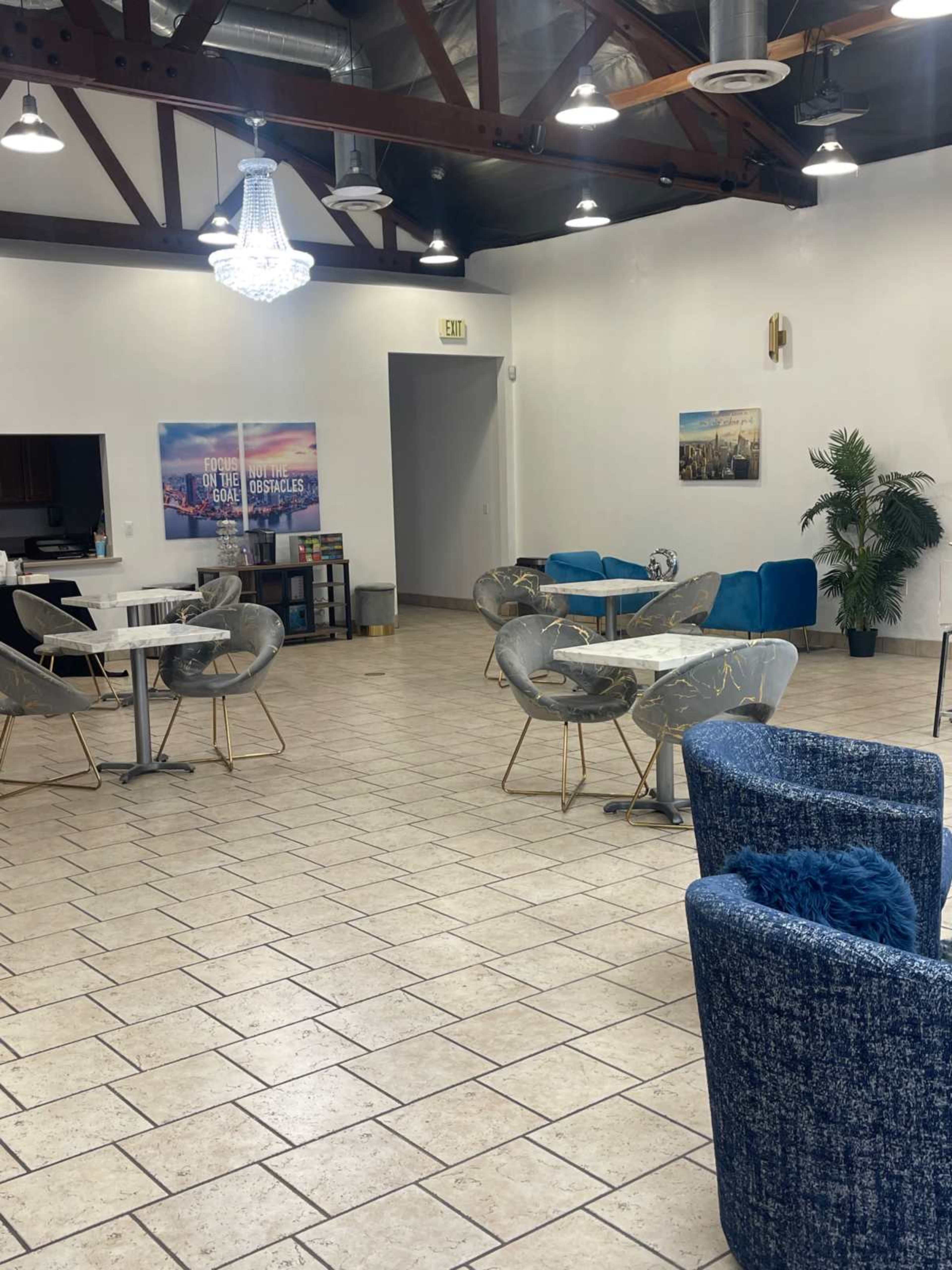 A spacious, well-lit café interior with modern furniture, including tables and chairs, and decorative plants.