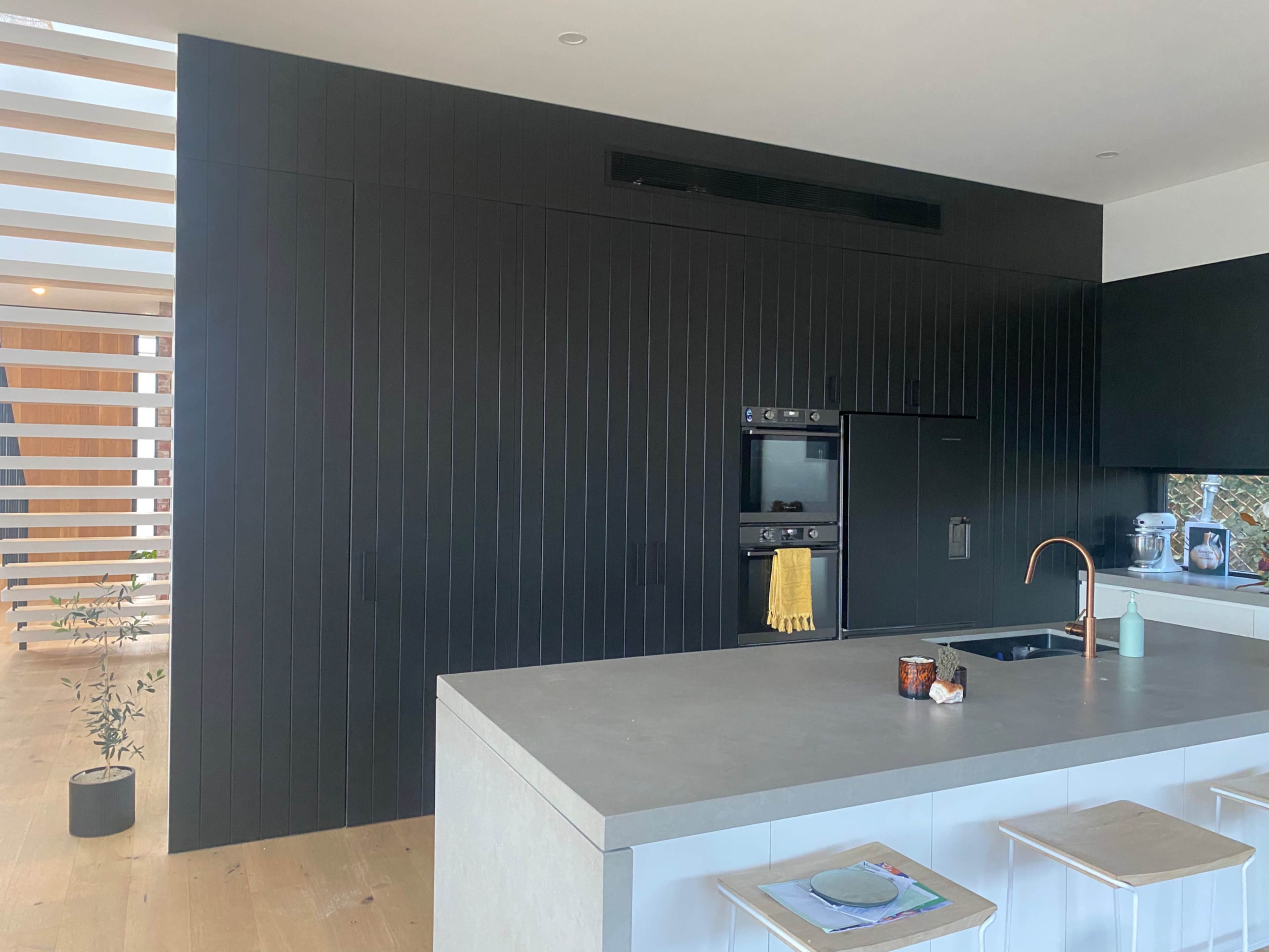 A modern kitchen with a black paneled wall, a gray island counter, and minimalistic stools.