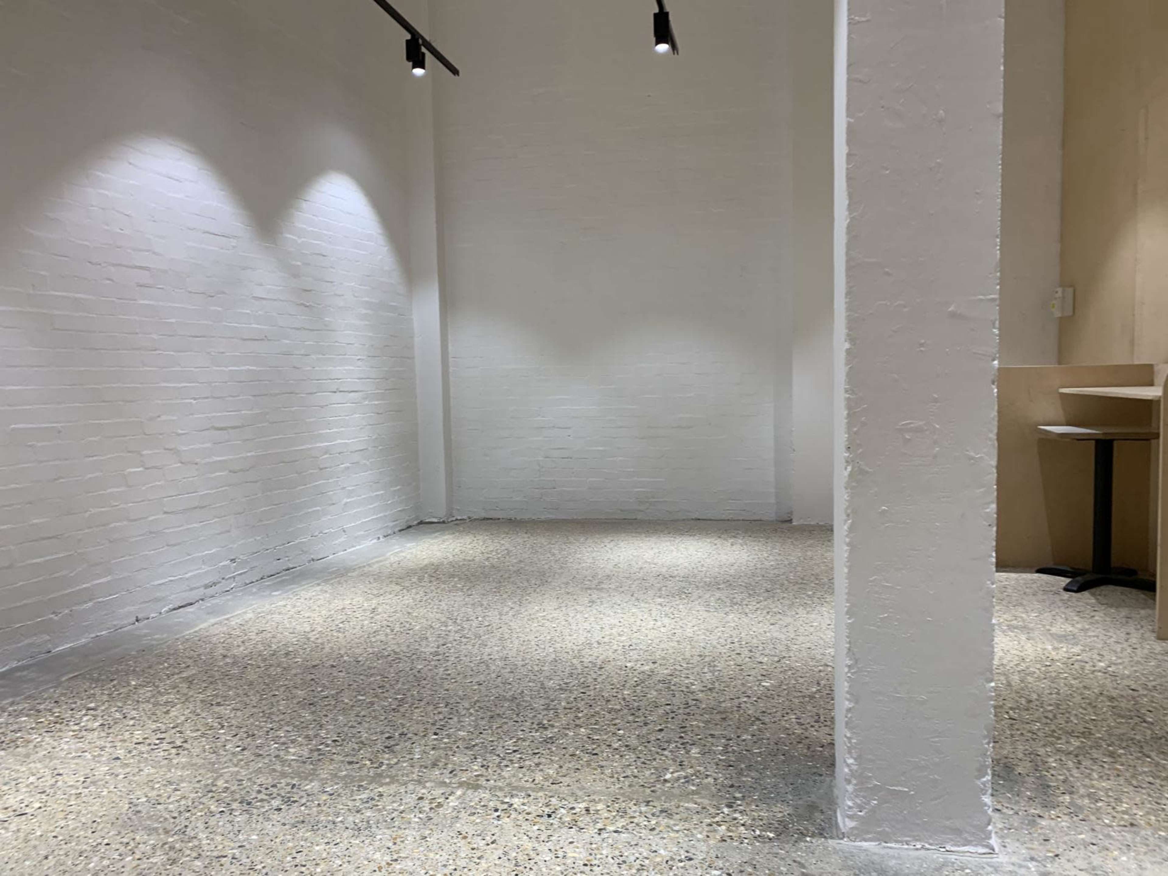 A minimalist, empty room with white walls, a concrete floor, and a single column.