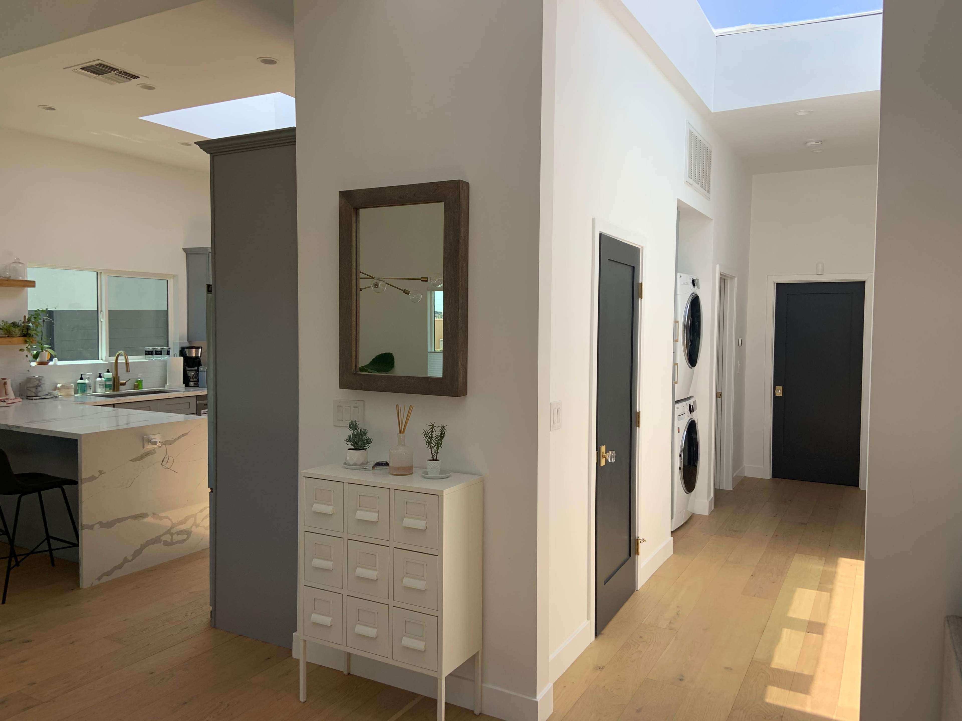 A modern interior space with a hallway leading to various rooms, including a kitchen on the left and a laundry area with stacked appliances on the right.