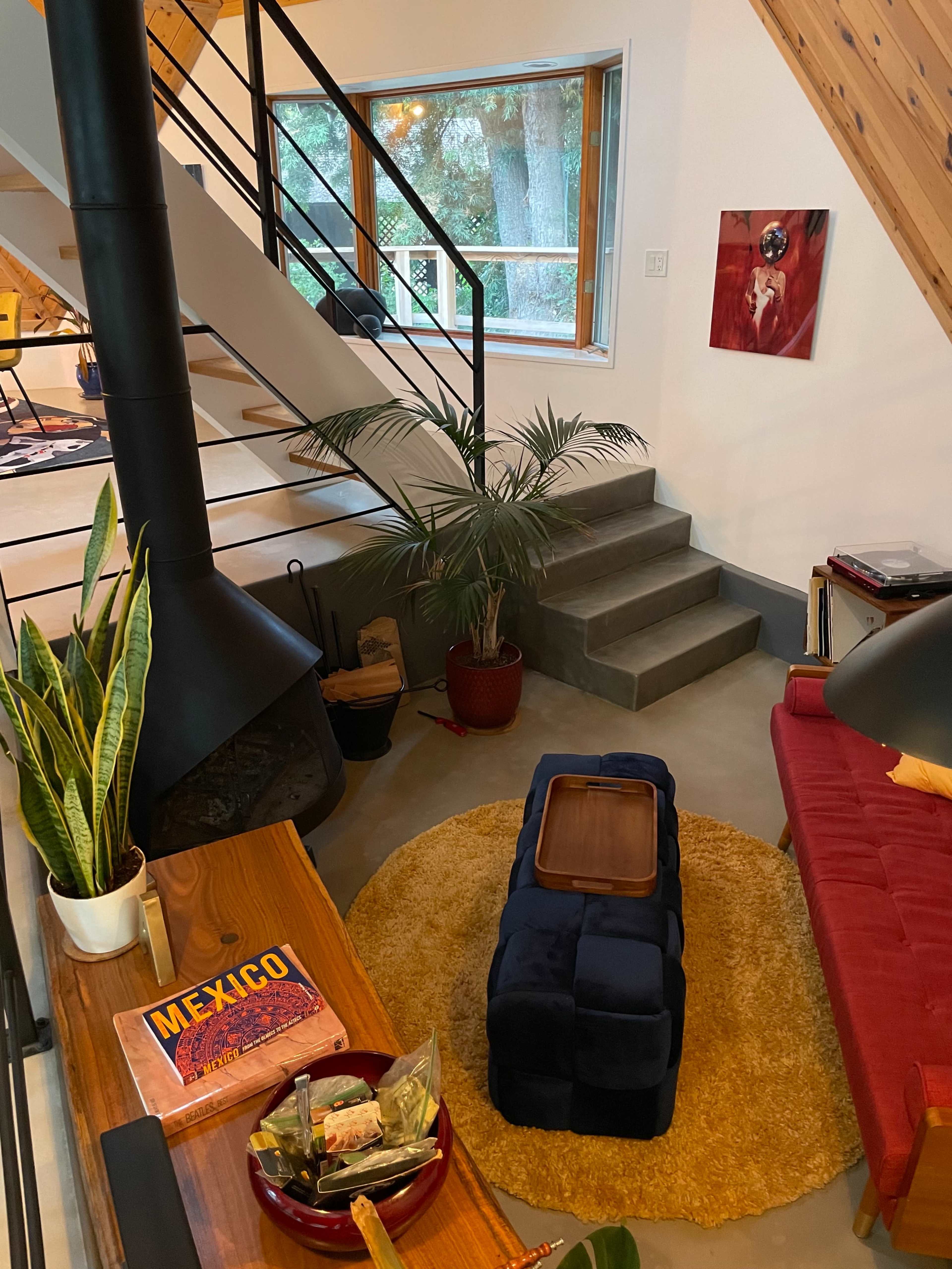 A modern living space with a red couch, a round rug, a wooden coffee table, and a staircase leading to an upper level.