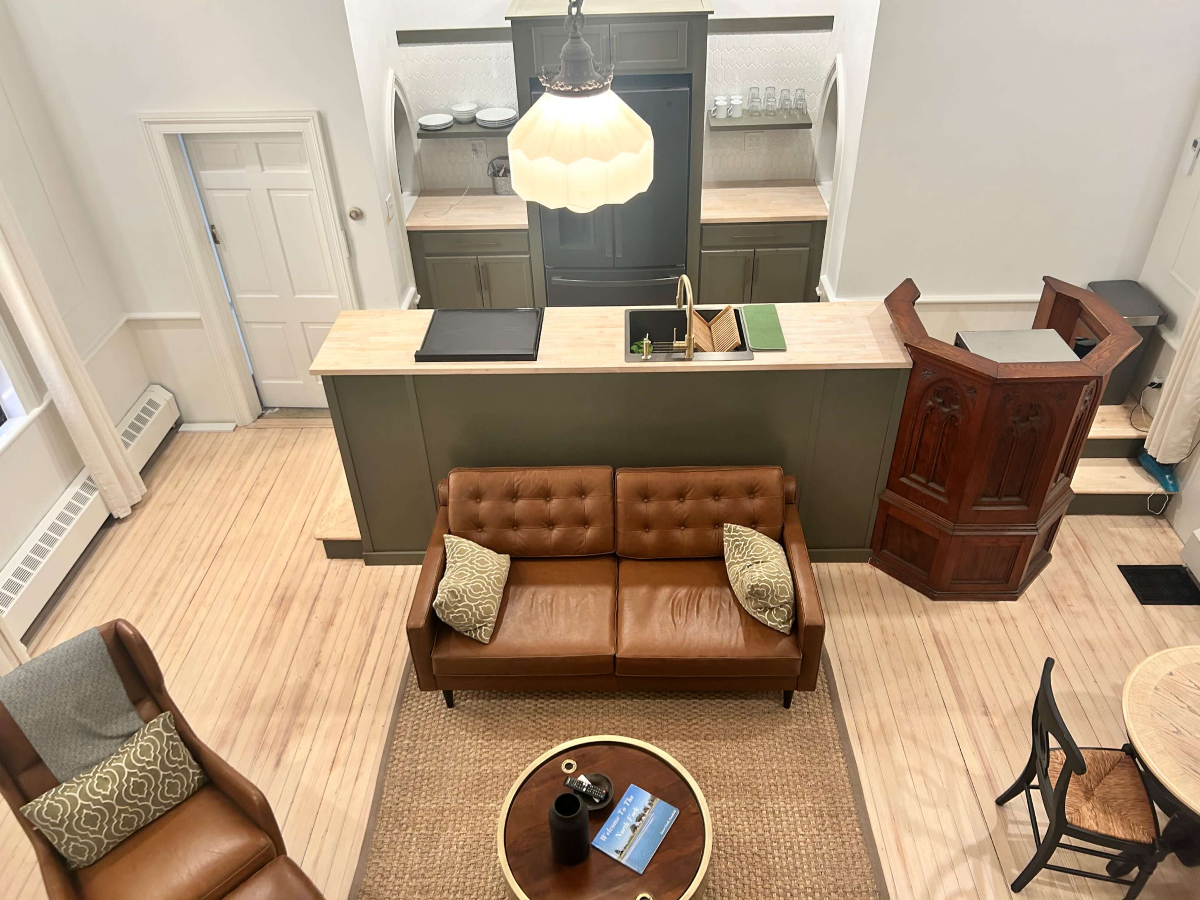 A modern living space with a kitchen area, featuring a brown leather couch, a round coffee table, and wooden cabinetry.