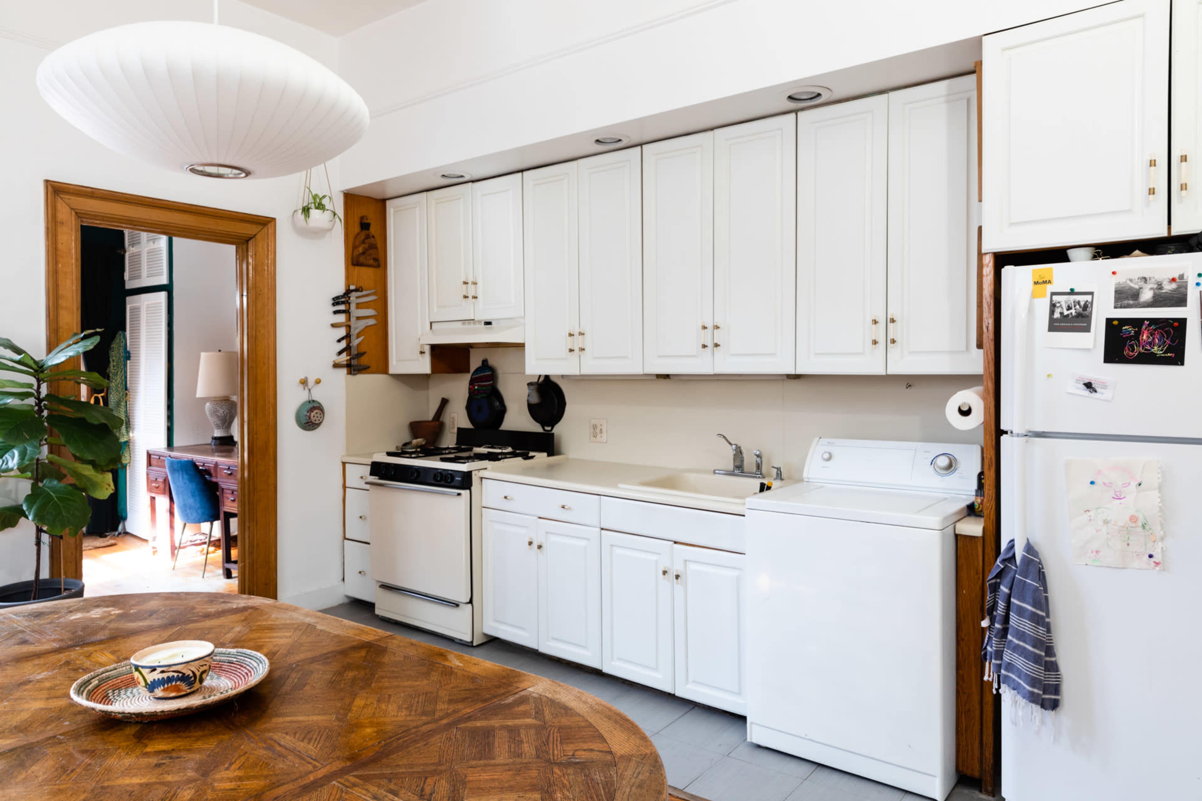 A kitchen with white cabinetry, a stove, a washing machine, and a round wooden dining table in the foreground.