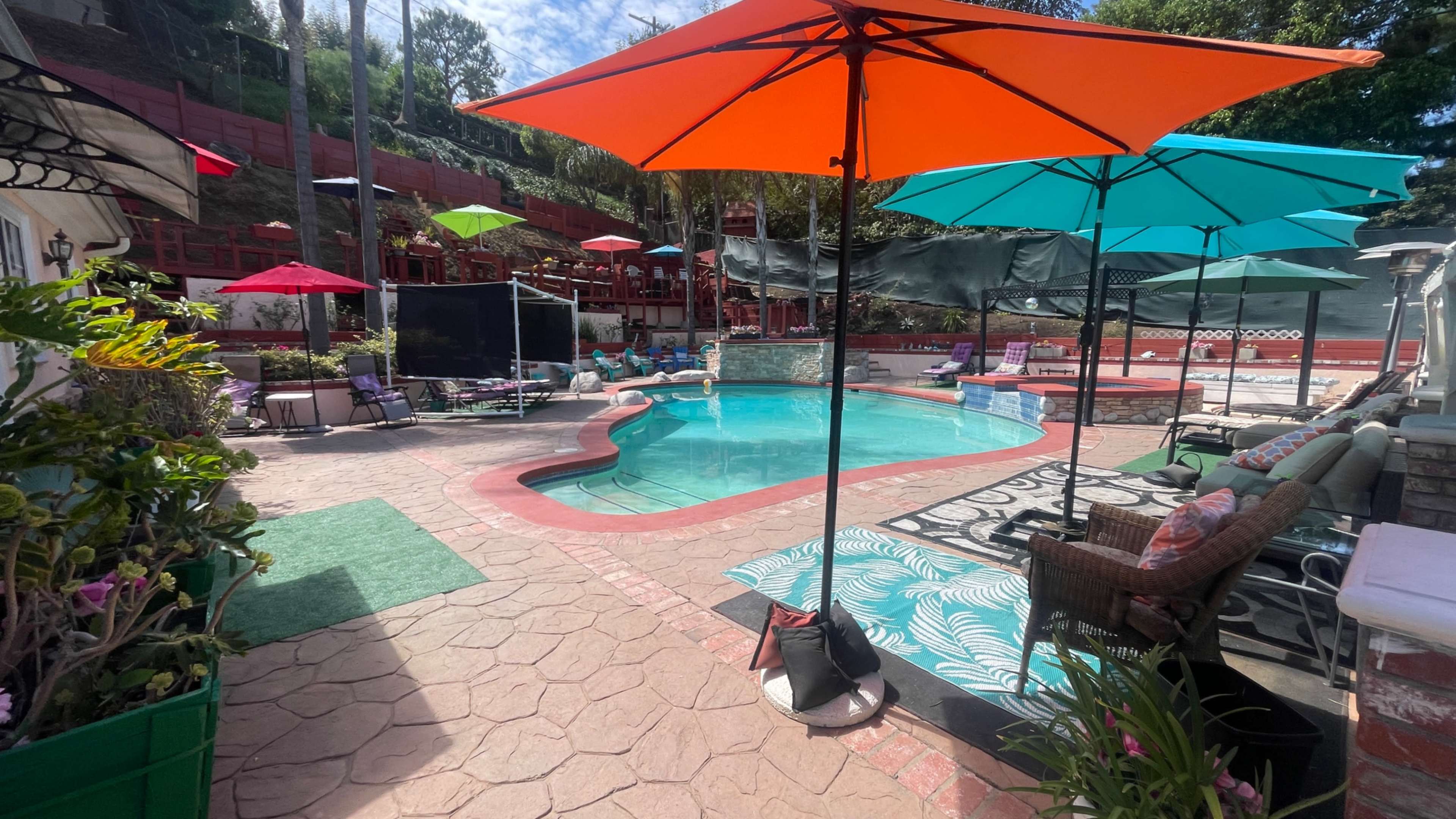 The image shows a colorful backyard pool area with umbrellas, lounge chairs, and decorative landscaping.