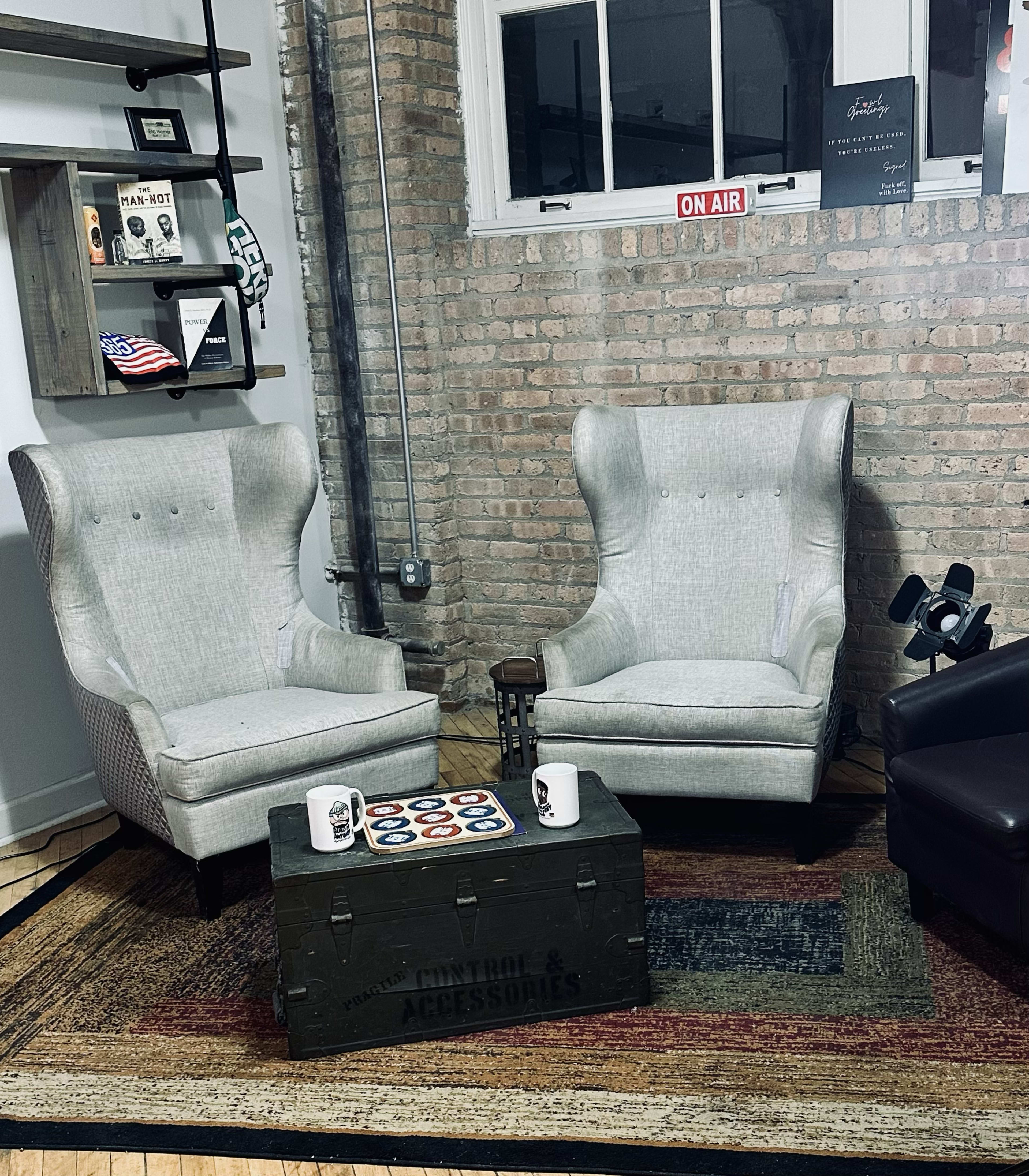 The image shows two wingback chairs facing each other over a small table in a room with a brick wall and a window.