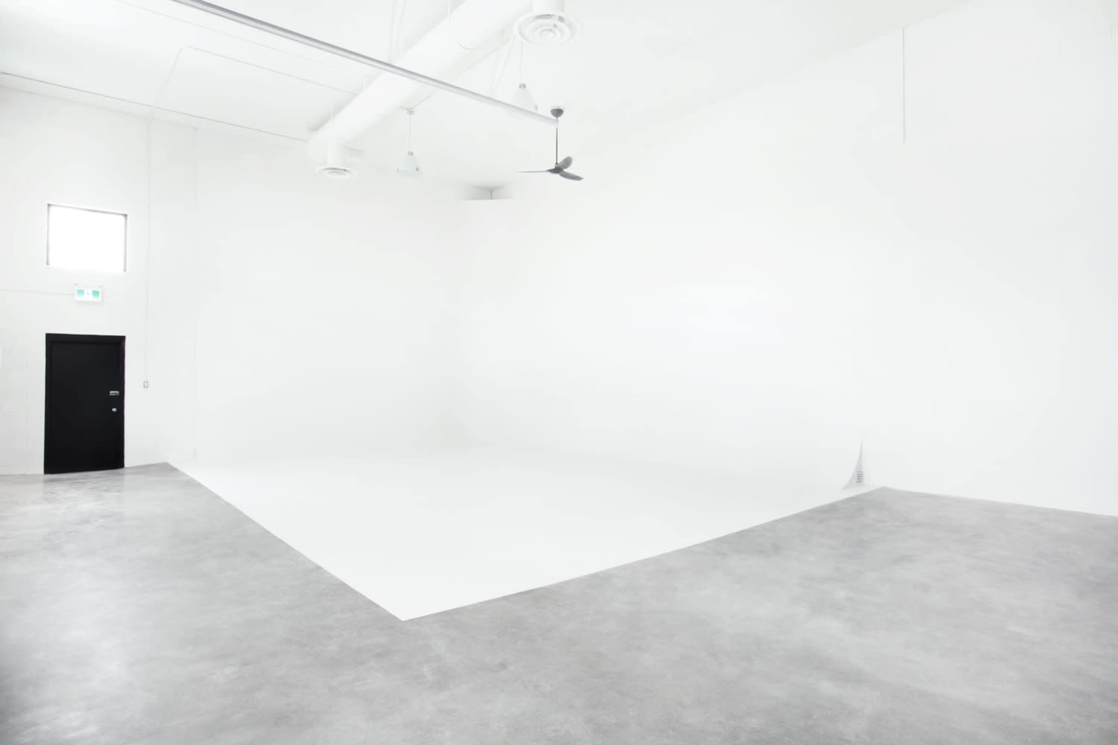 A spacious, minimalist room with white walls, a concrete floor, and a large, empty area.