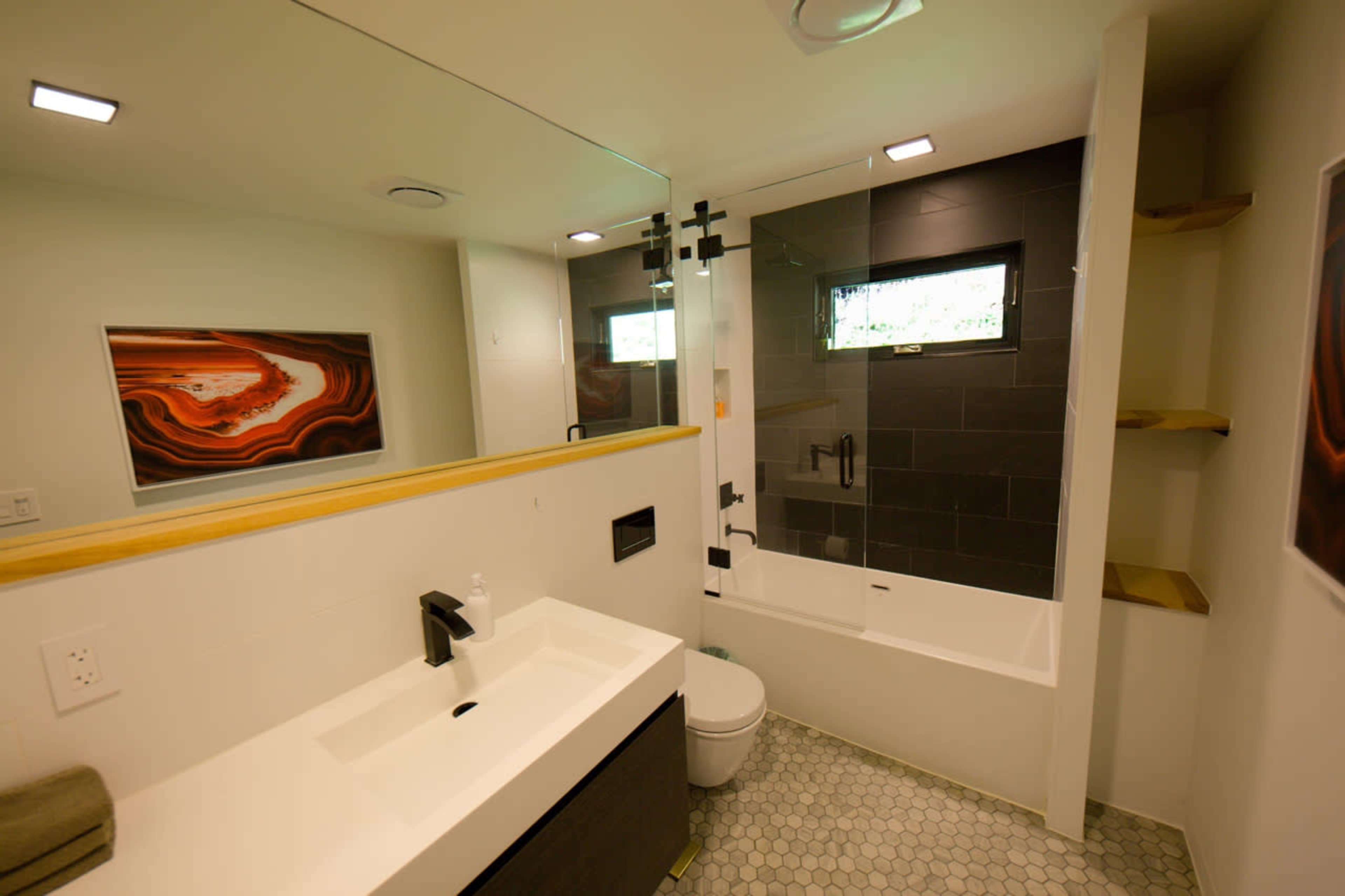The bathroom features a modern design with a white sink, a bathtub with a glass shower enclosure, and a large mirror above the vanity.