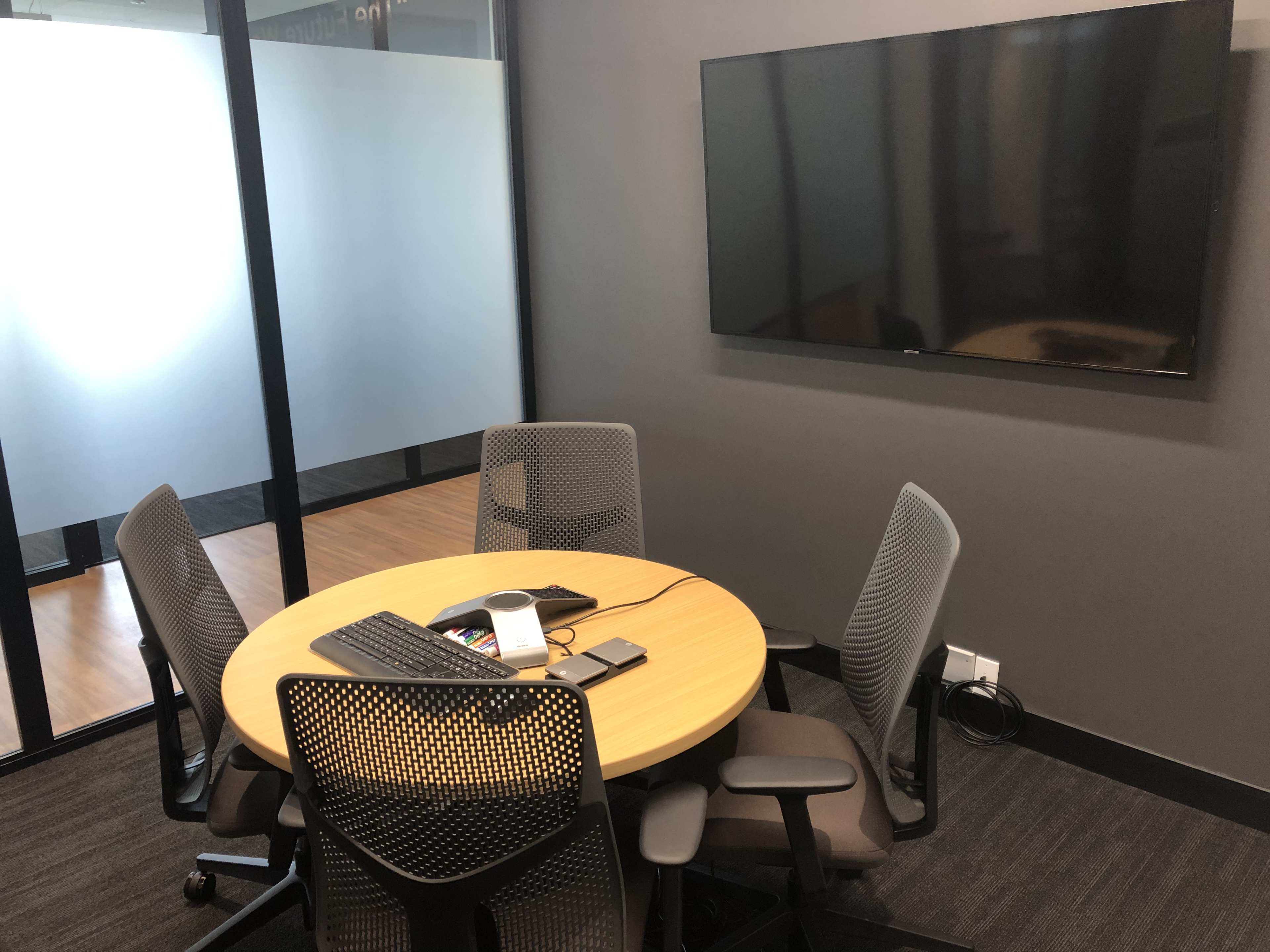 A small meeting room features a round table with four chairs and a wall-mounted television.