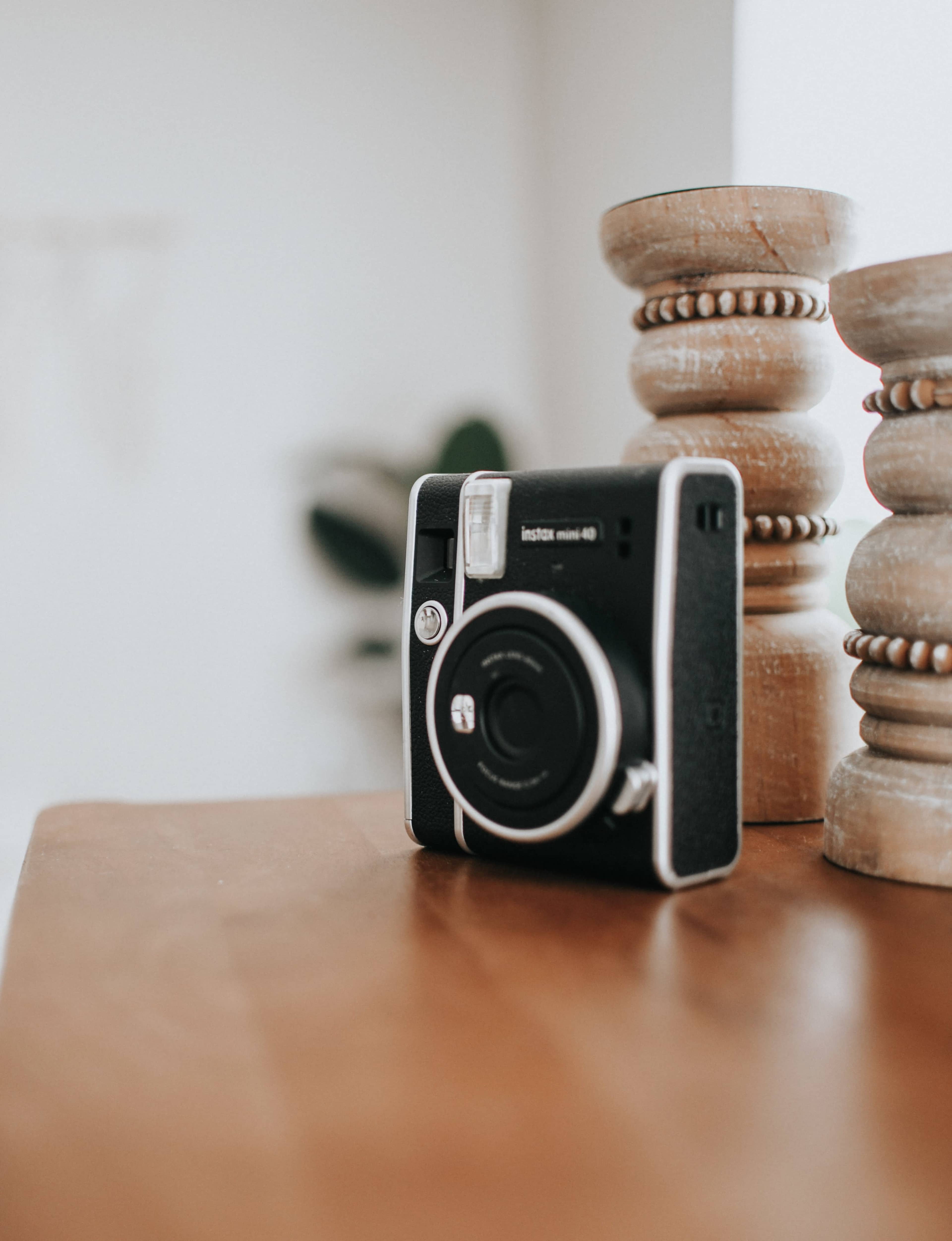 A black instant camera is placed on a wooden surface next to two decorative wooden pillars.