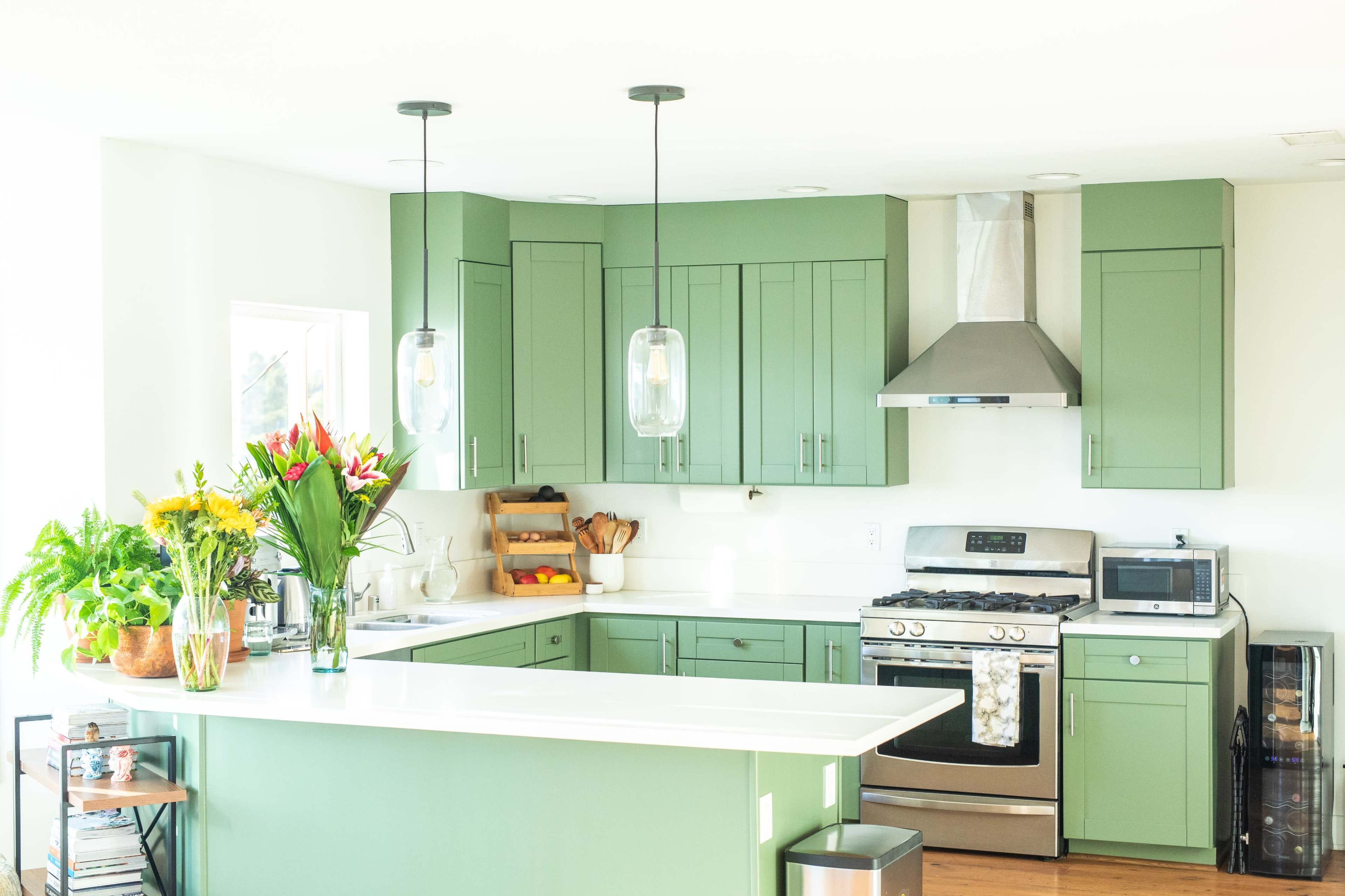 The kitchen features green cabinetry, a stainless steel stove, a white countertop, and a wooden island with plants and flowers.