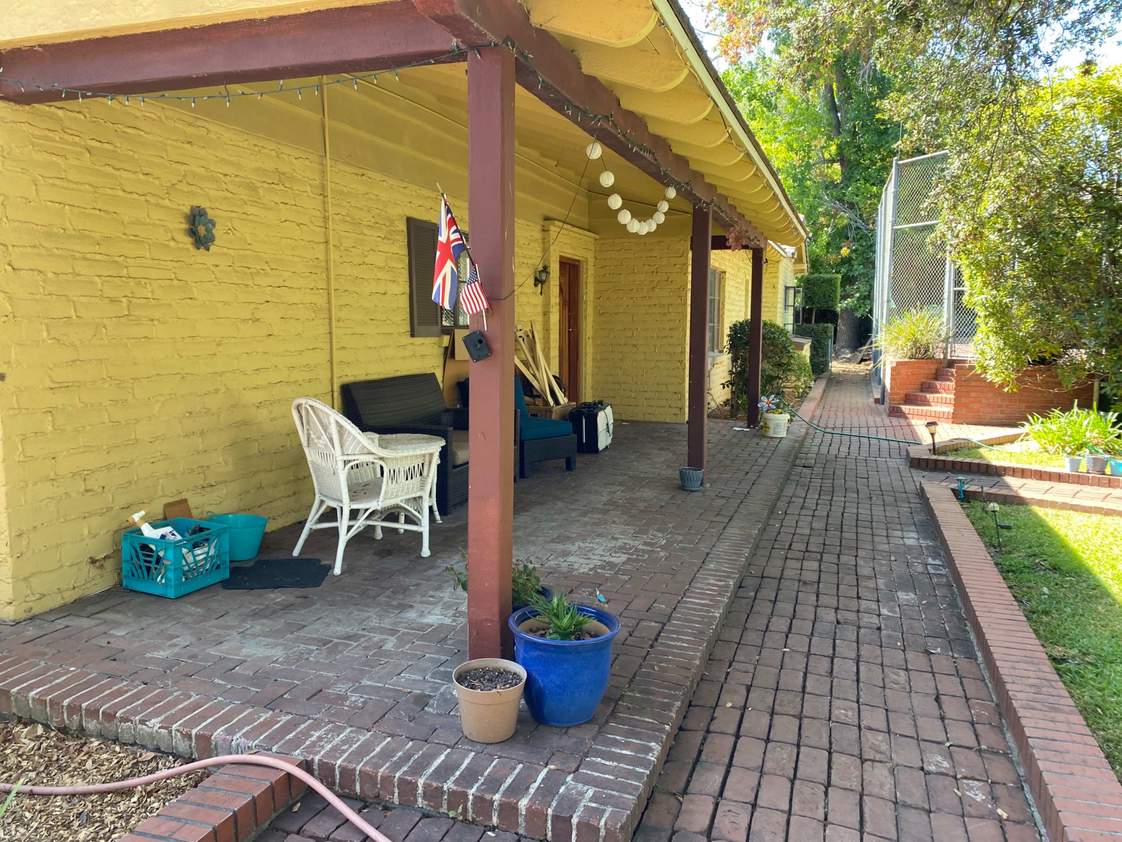 A covered porch with a seating area, a British flag, and a pathway leading to a garden bordered by brick.