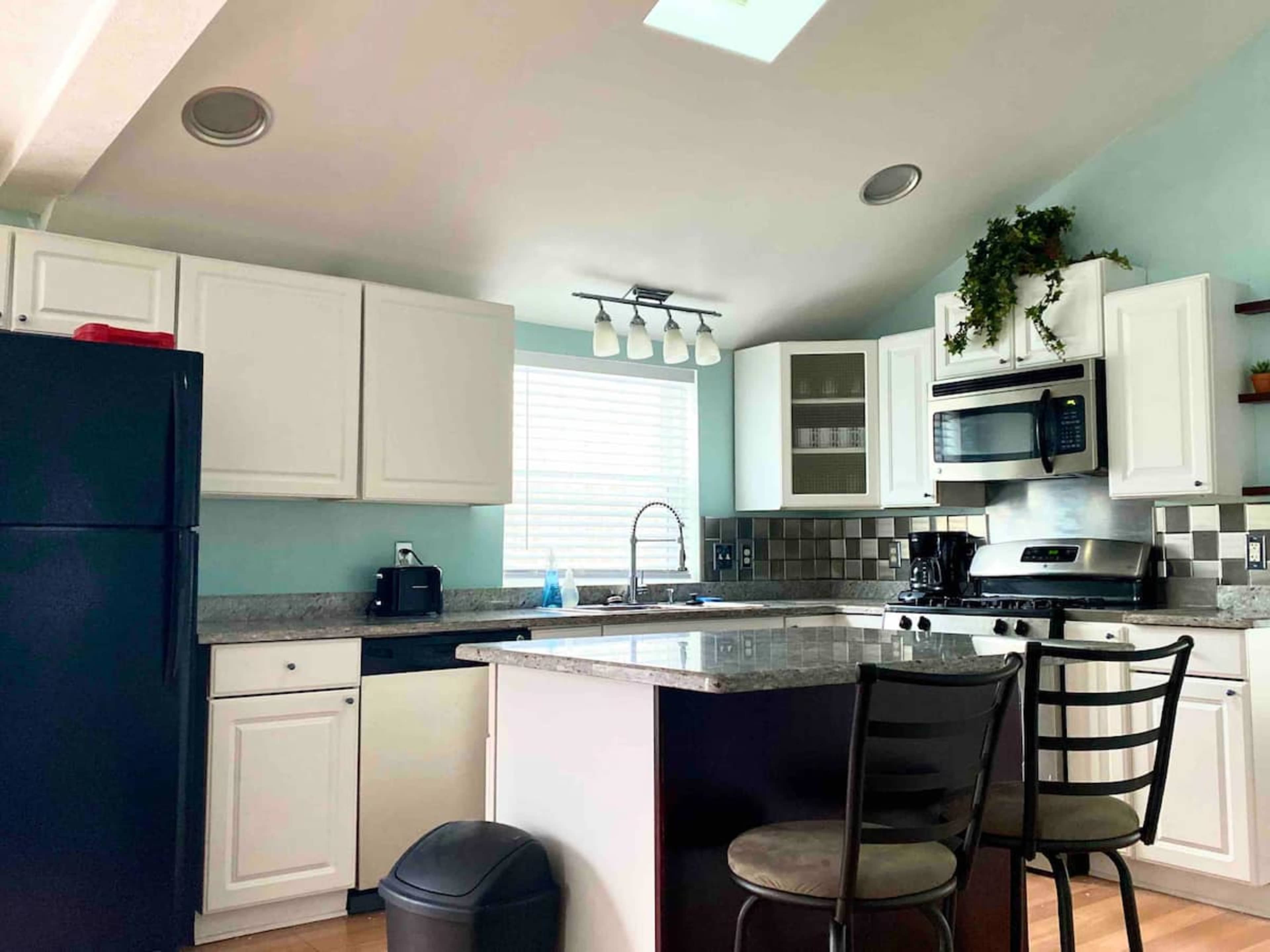 A modern kitchen with white cabinets, a granite countertop, a black refrigerator, and stainless steel appliances.