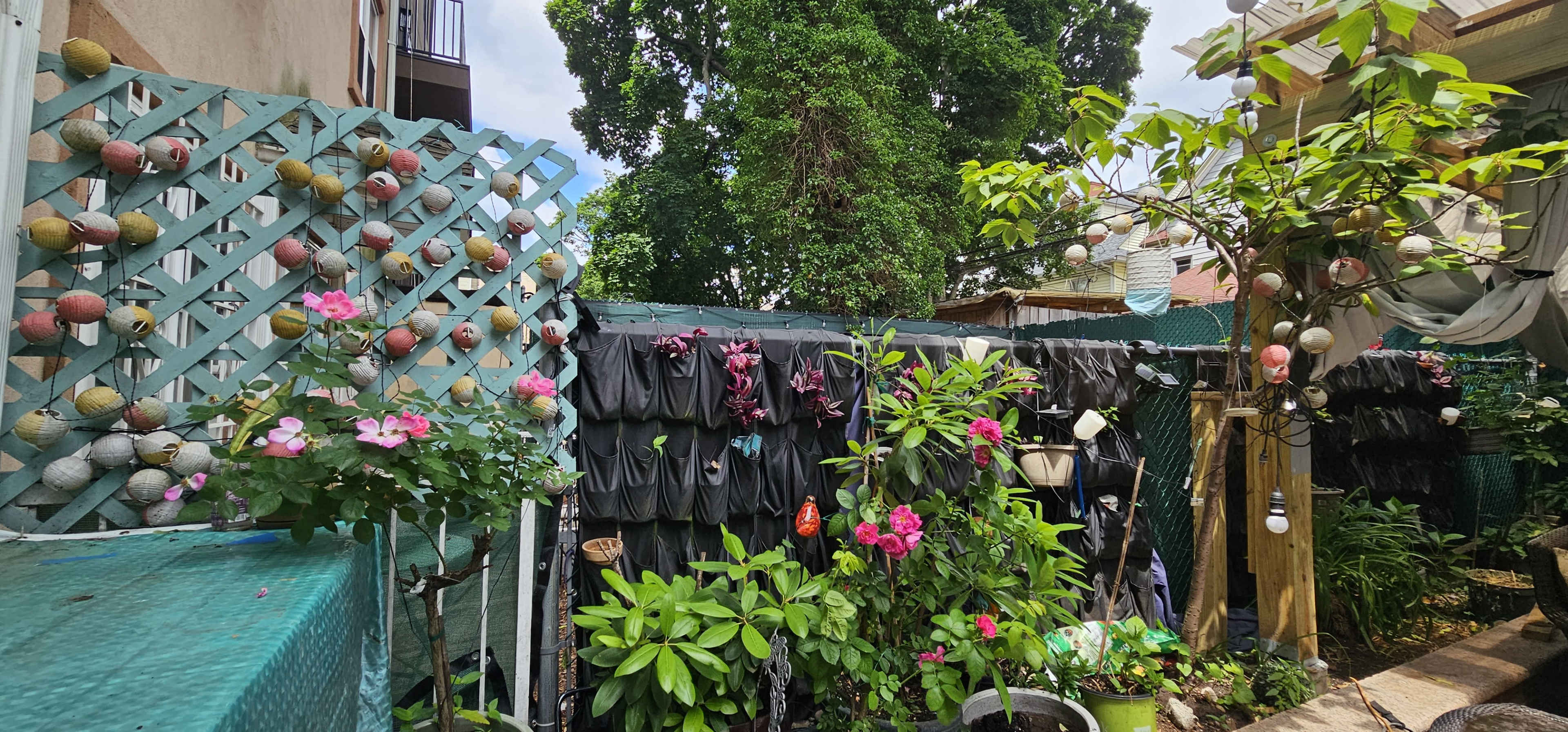 A garden area featuring vertical plant displays with colorful flowers, surrounded by green foliage, garden decor, and a lattice structure.