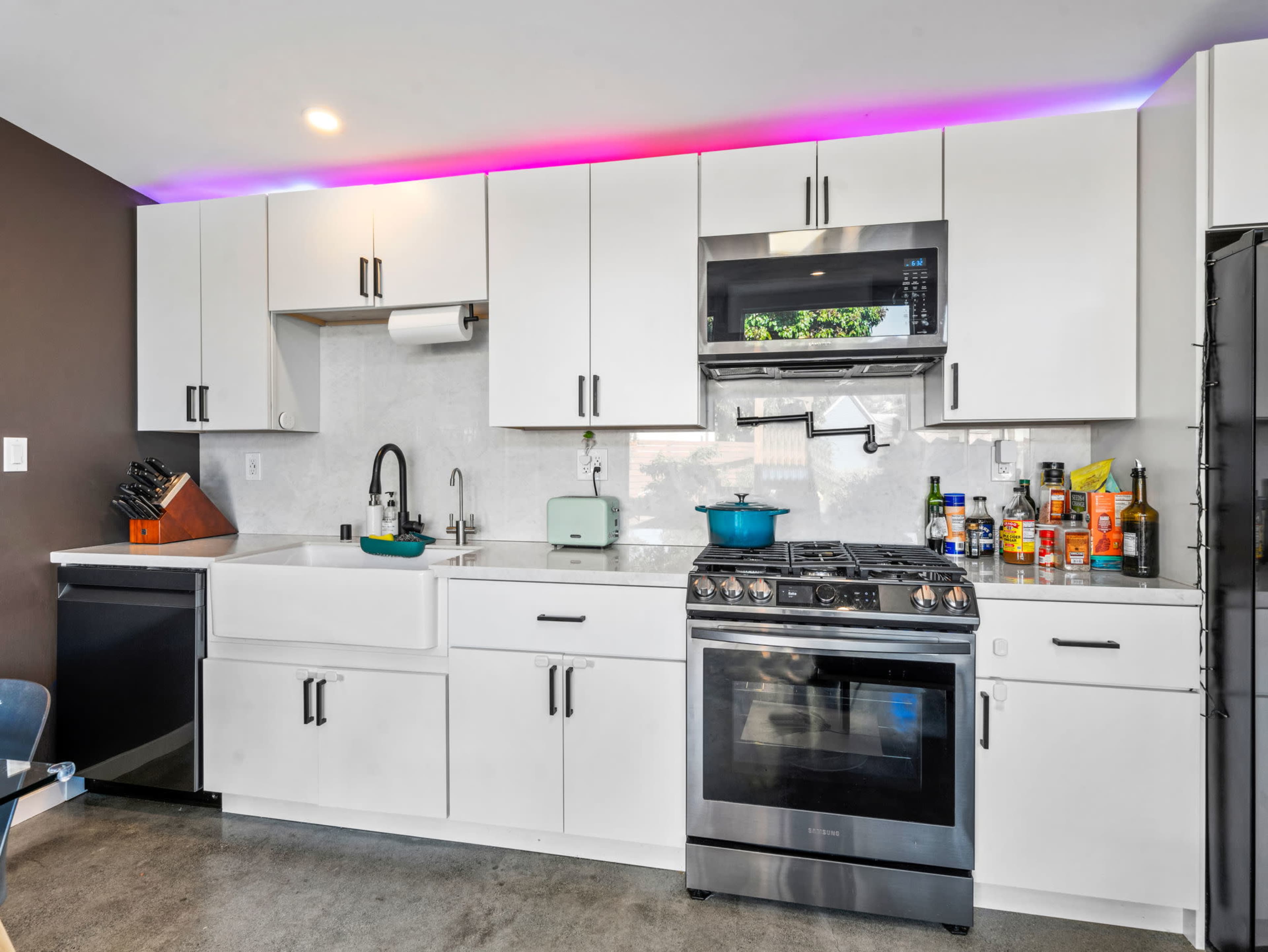 A modern kitchen features white cabinets, stainless steel appliances, and a colorful LED light strip along the upper edge.
