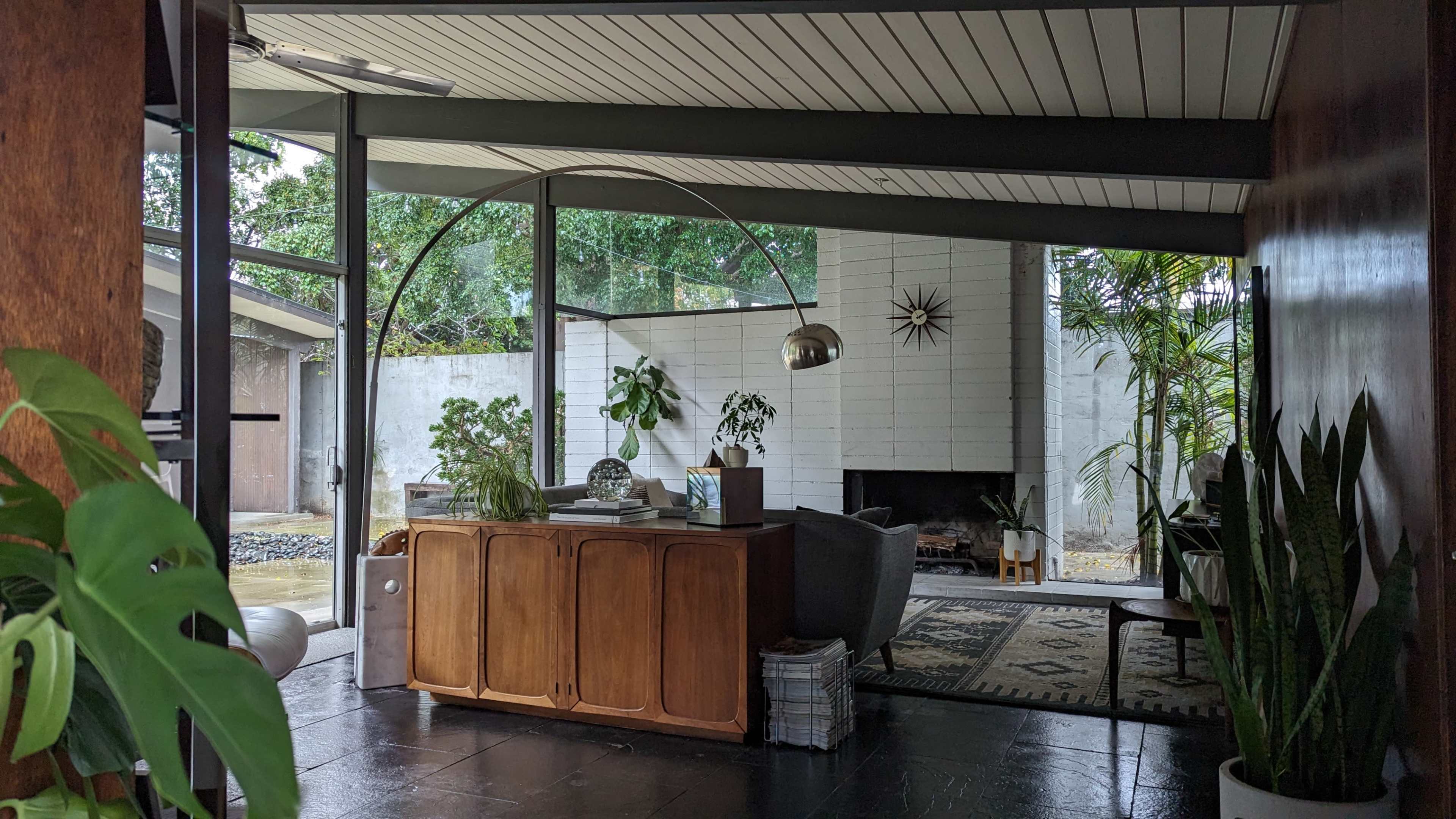 A modern interior with a wooden cabinet, a gray chair, a fireplace, and large windows allowing natural light to enter.