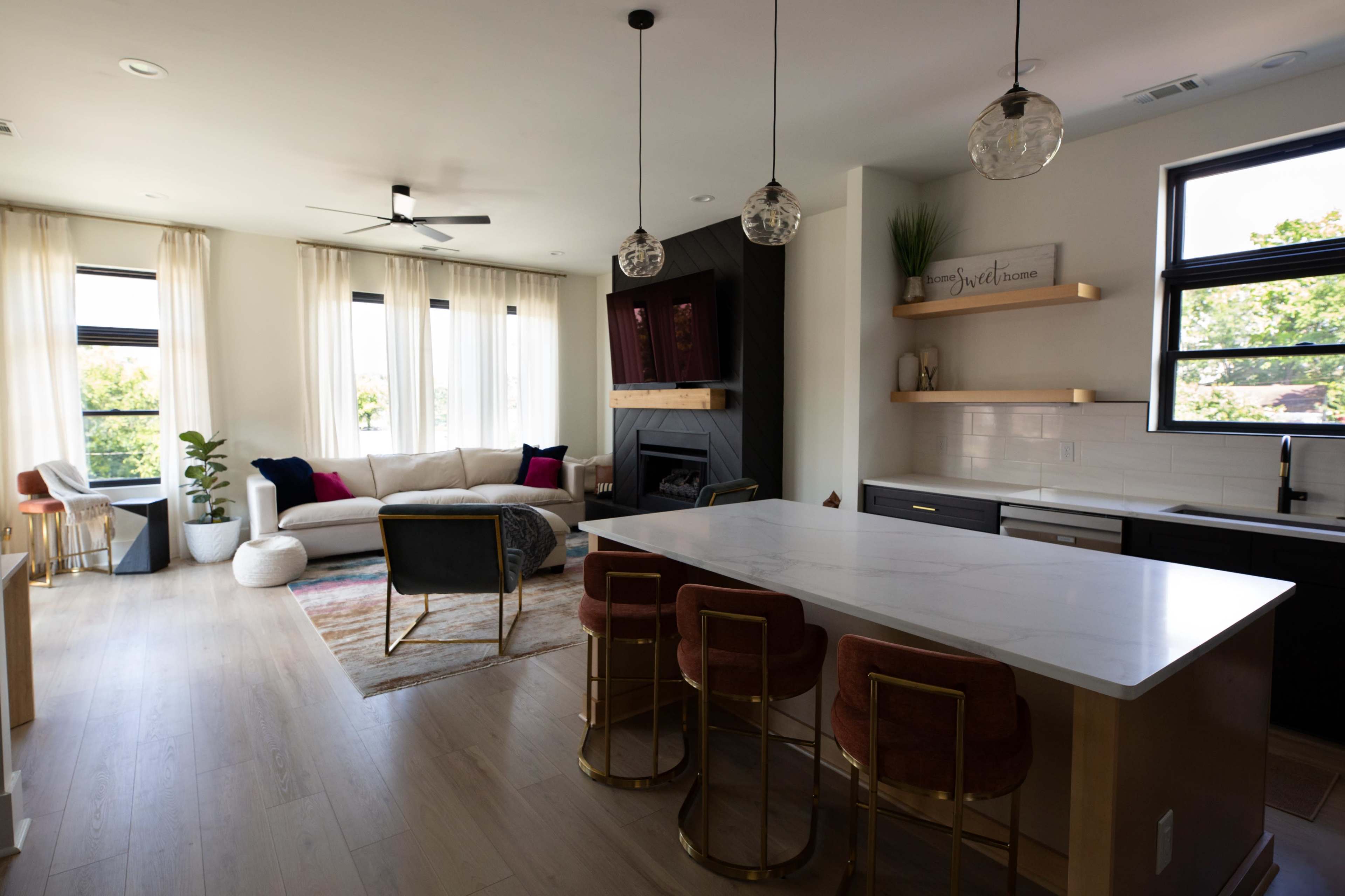 The image shows a modern open-concept living space featuring a kitchen with a marble island, bar stools, and a cozy seating area with a sofa and decorative elements.