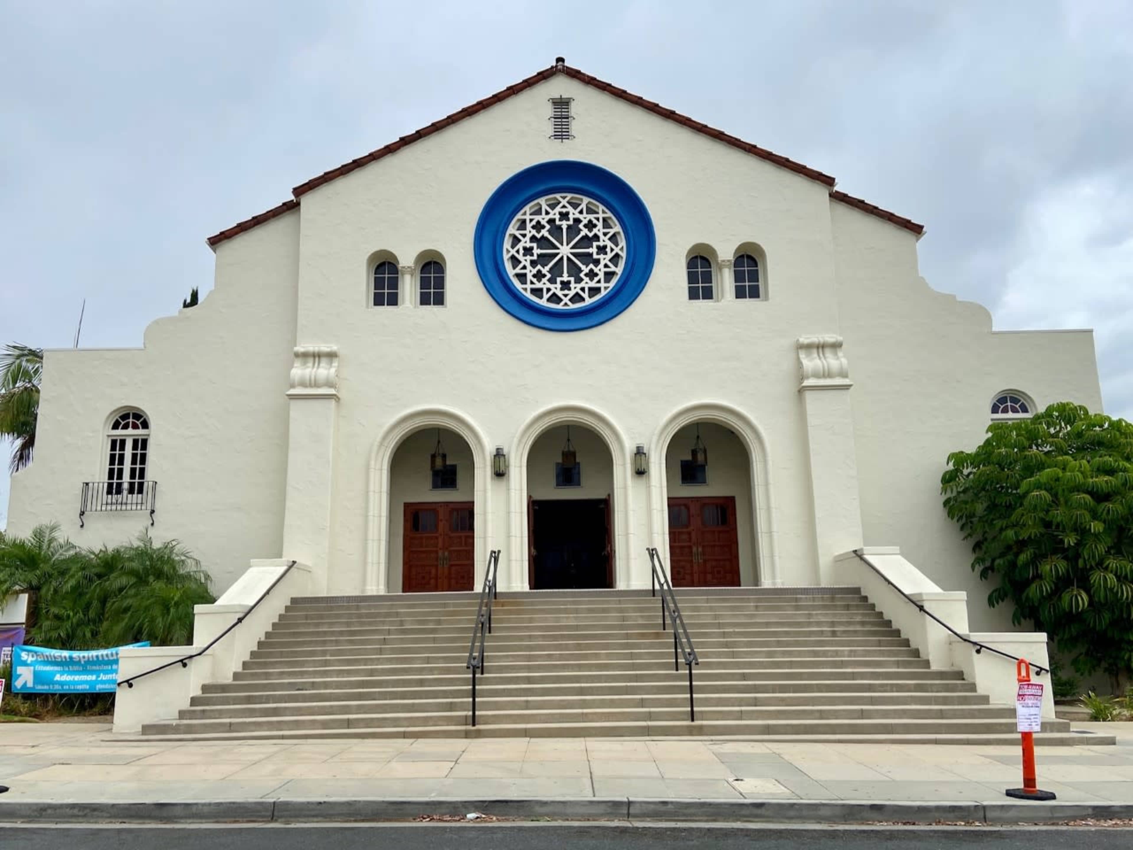 A large, white building with a distinctive circular window and two wooden doors, flanked by a flight of steps leading up to the entrance.