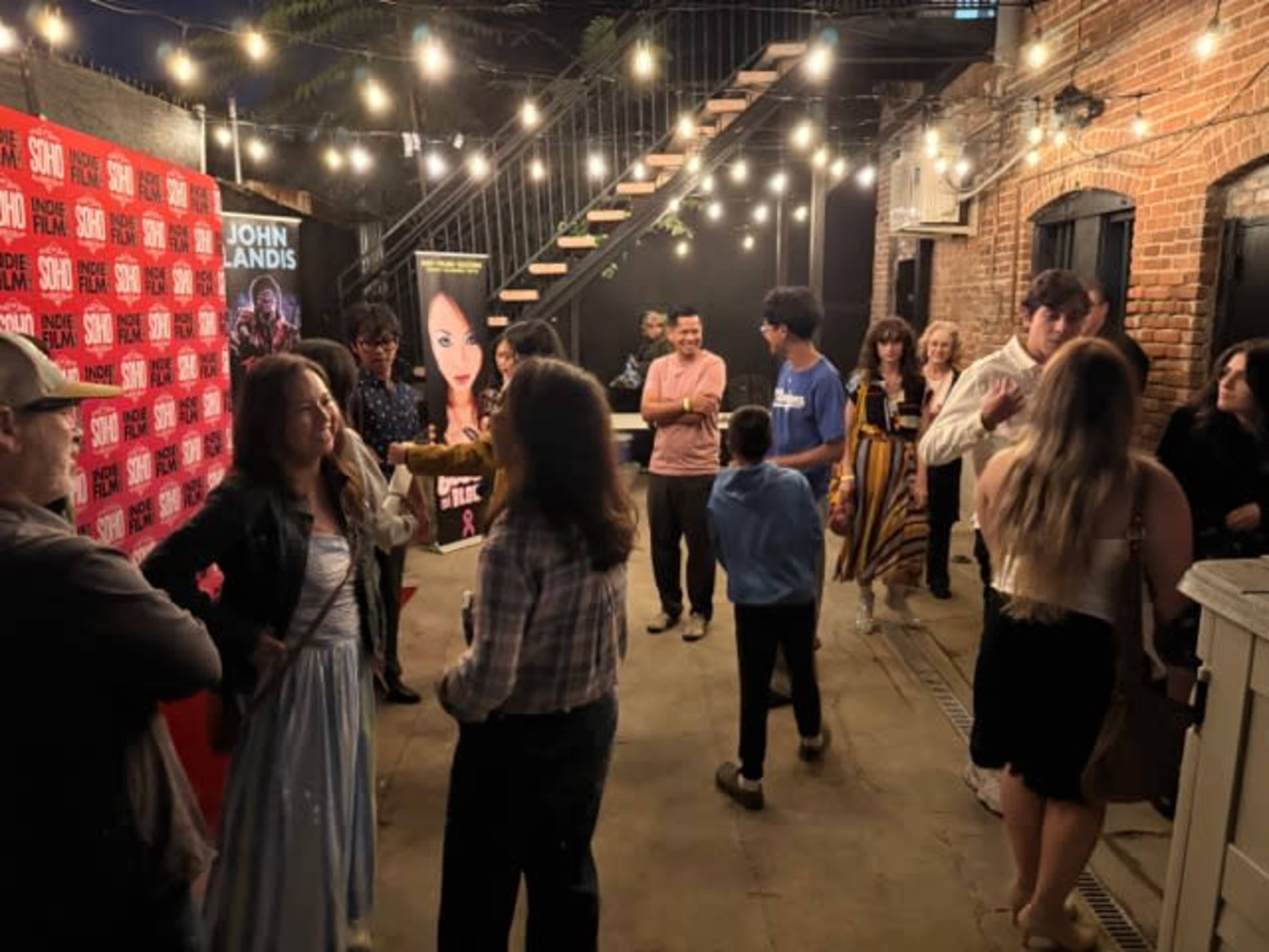 A crowd gathers outside a venue adorned with string lights and promotional banners.