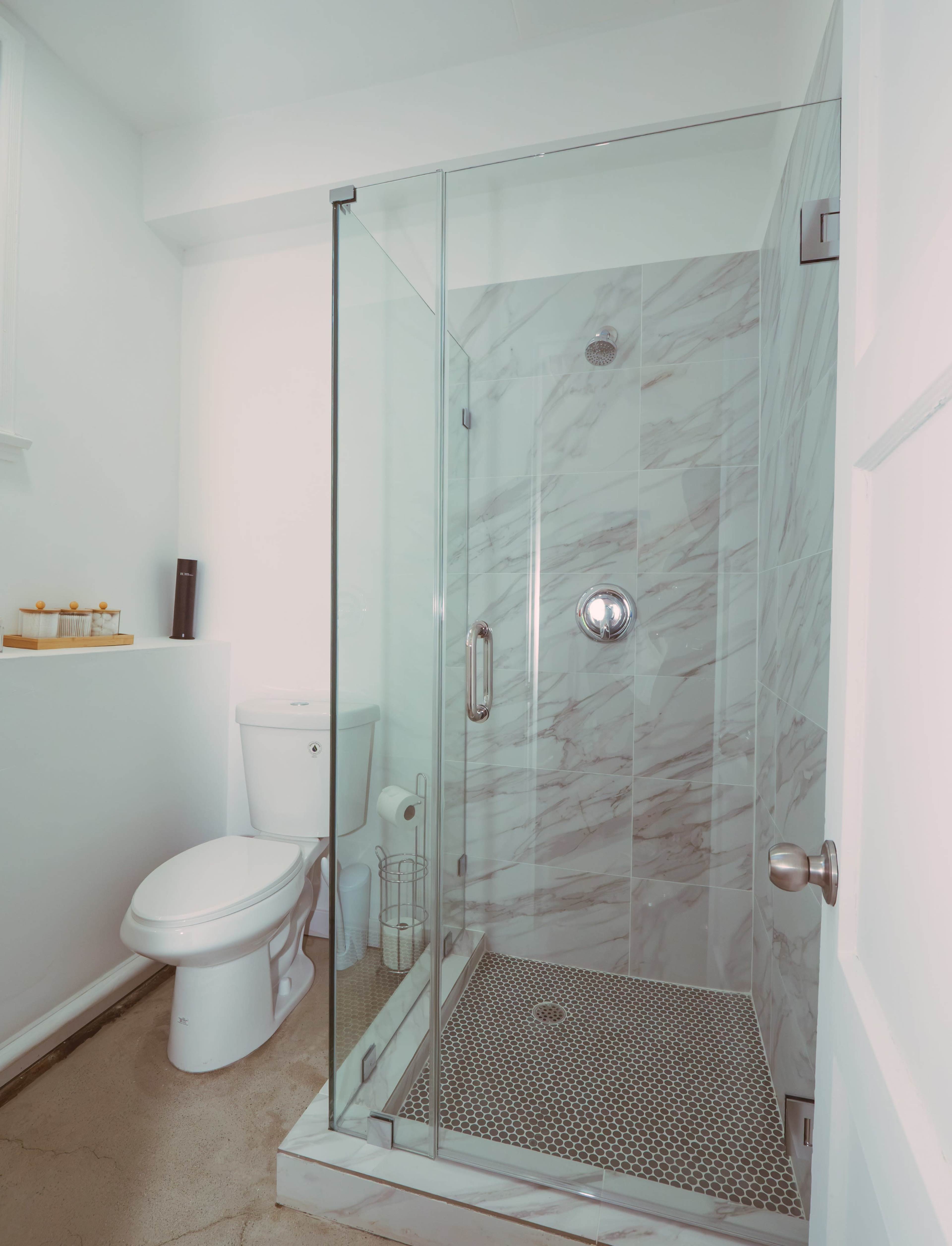 The image shows a modern bathroom featuring a glass shower enclosure, a toilet, and marble-patterned walls.