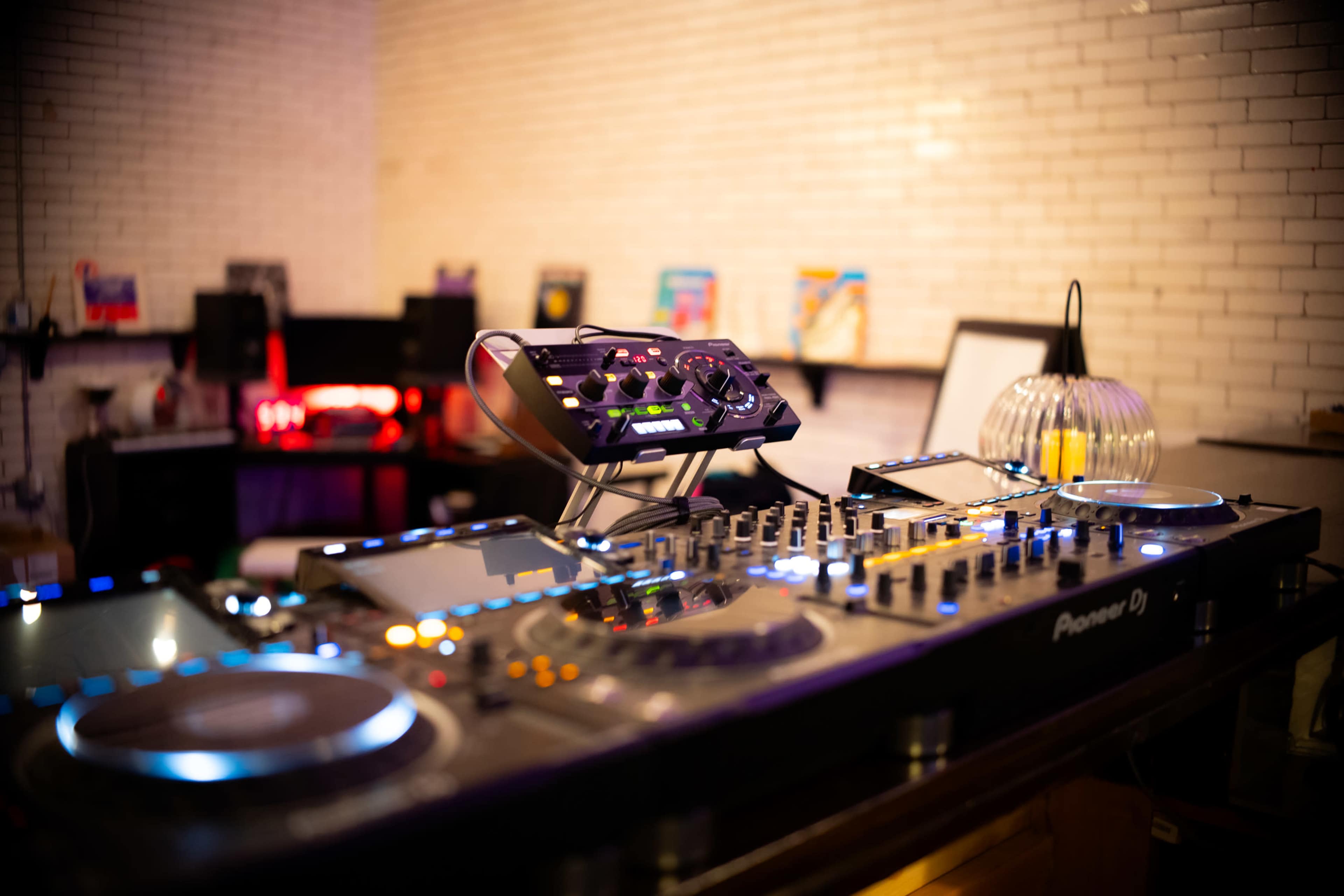 A DJ setup featuring a Pioneer mixing console is positioned on a countertop with various electronic devices and decor in the background.