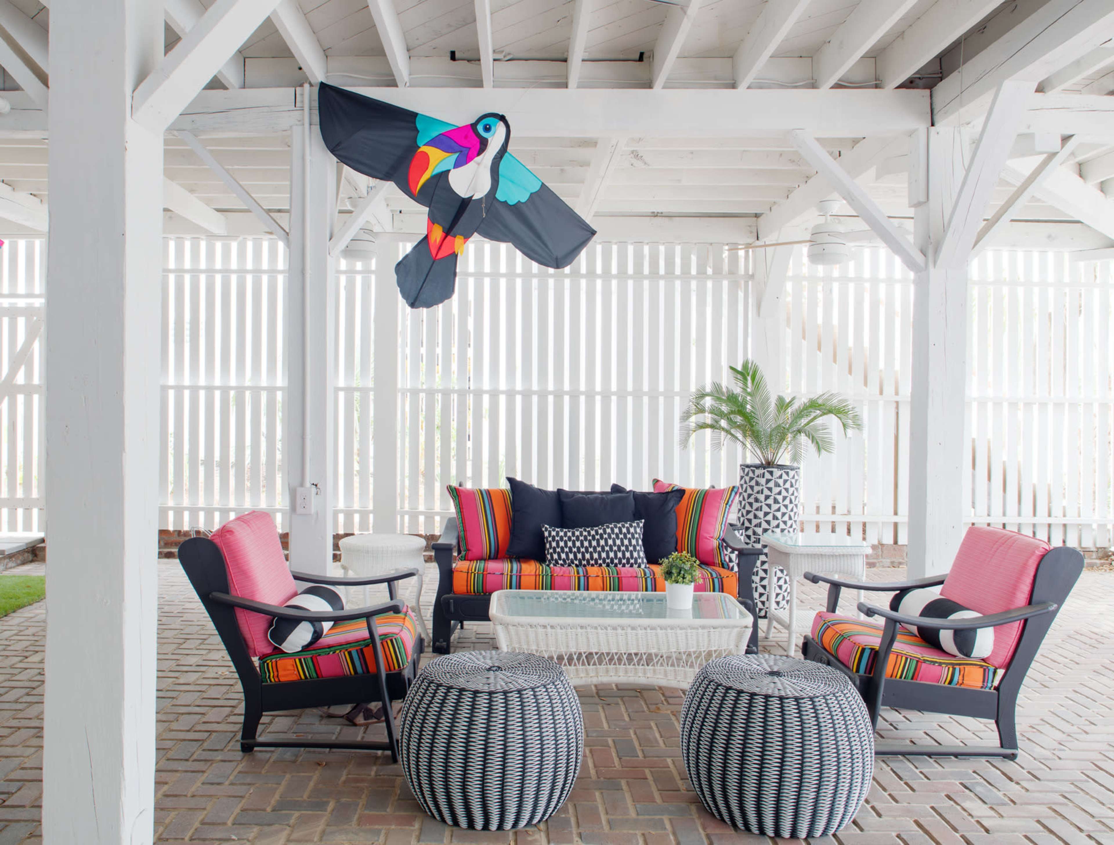 A colorful outdoor seating area features a striped couch and chairs with a toucan decoration hanging above.