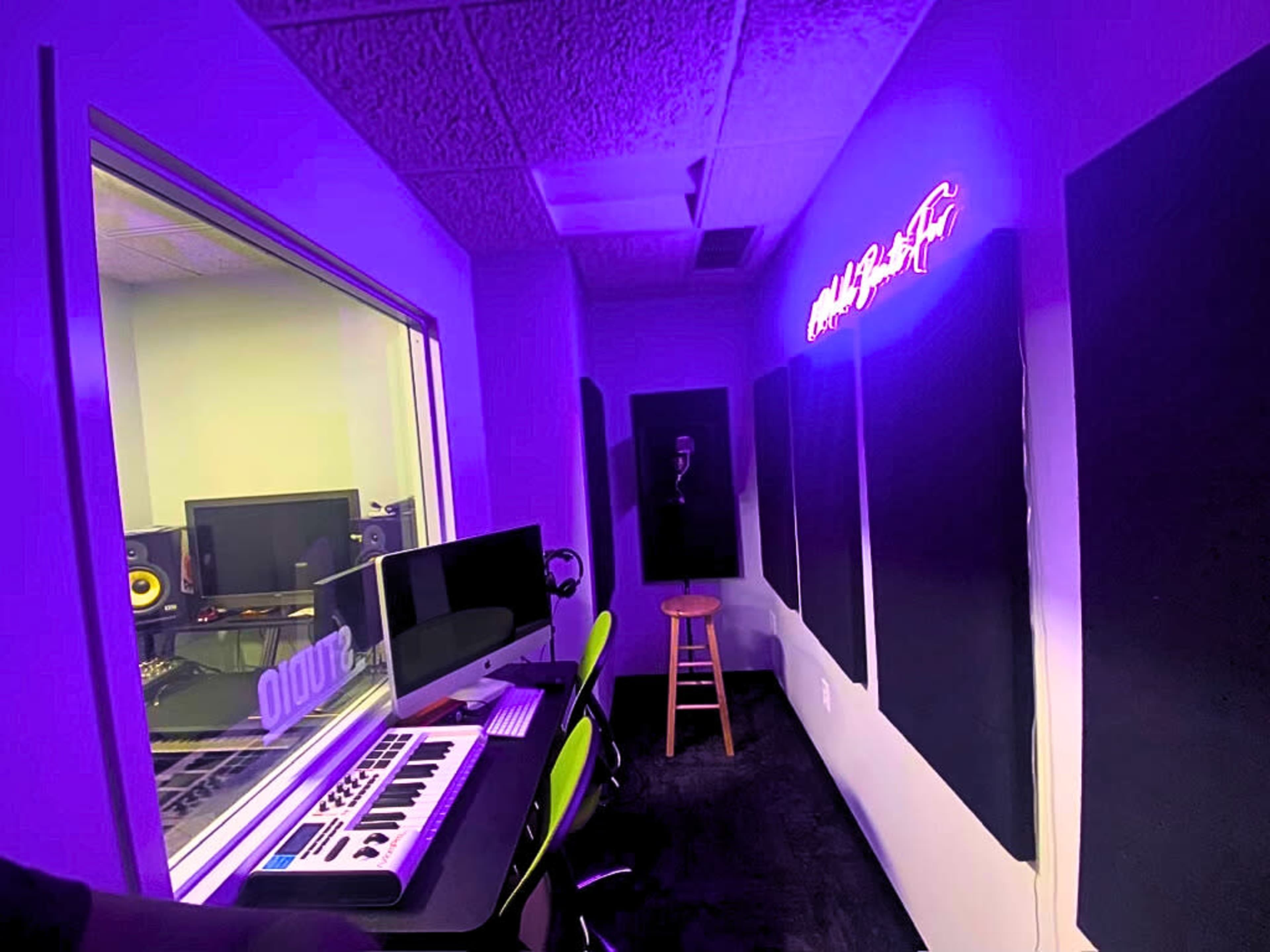 A music studio with monitors, a keyboard, and acoustic panels, illuminated by purple lighting.