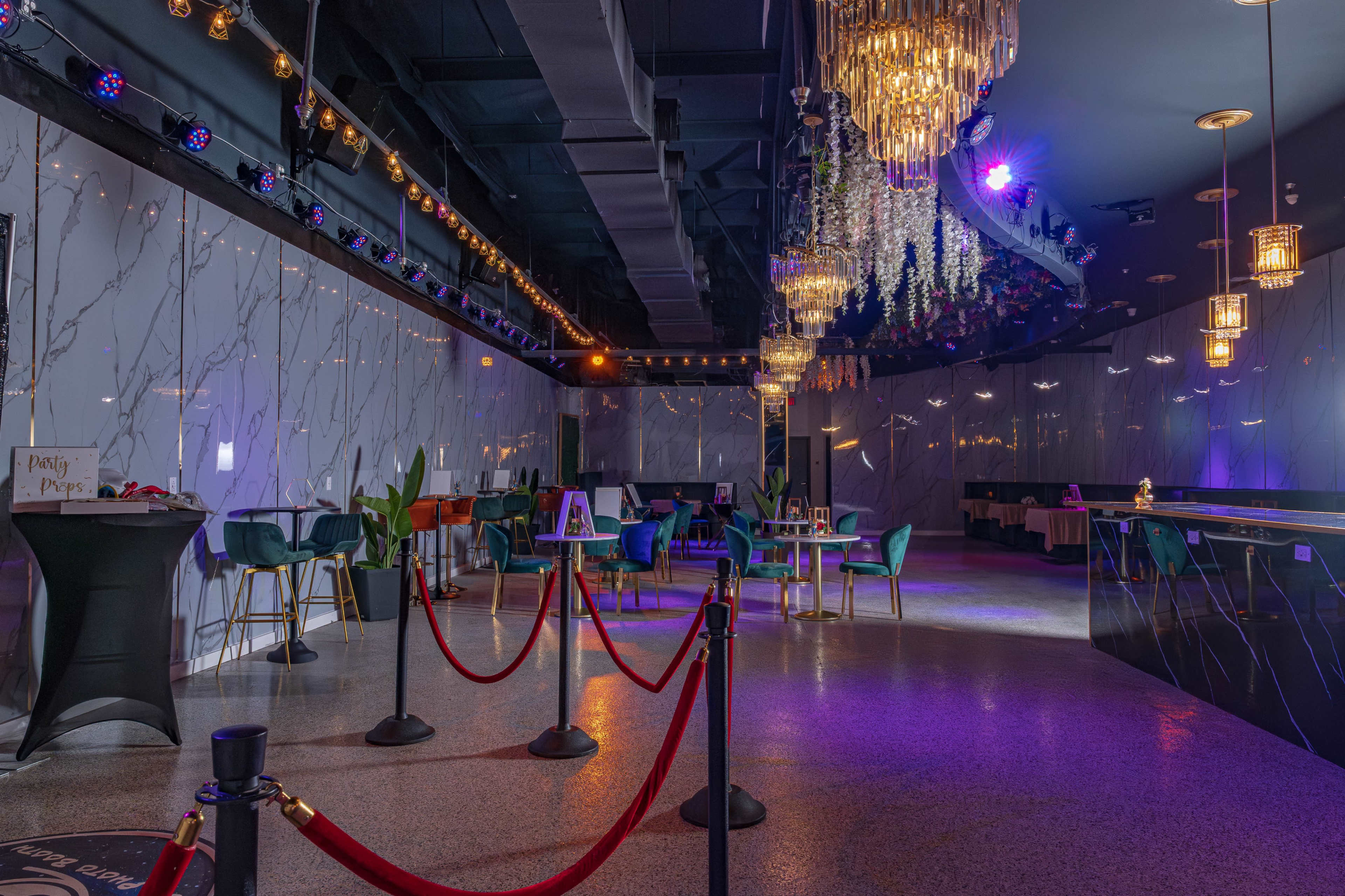 A modern event space features elegant decor with marble walls, colorful seating, a bar area, and soft lighting from chandeliers.
