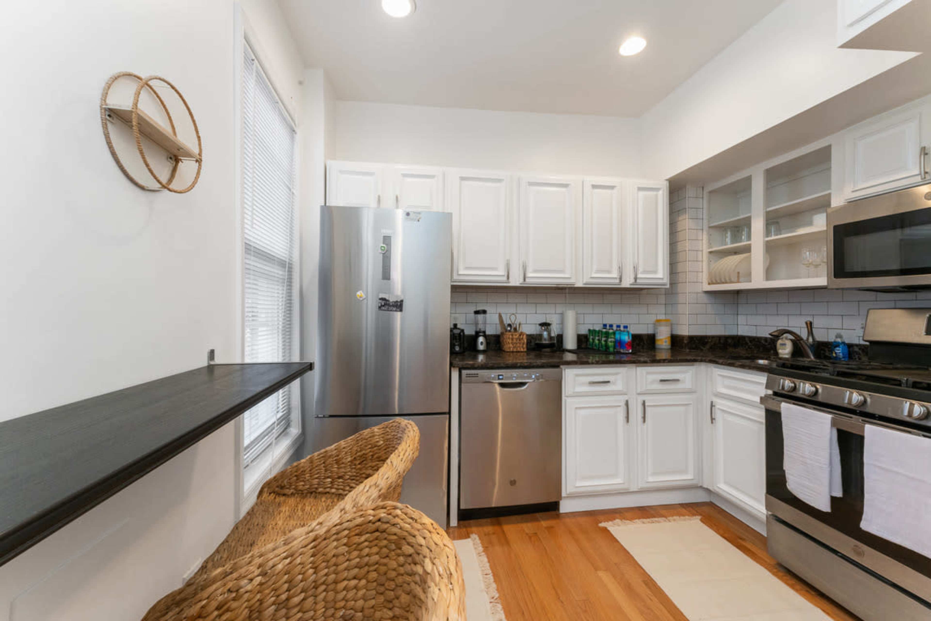 The kitchen features white cabinets, a stainless steel refrigerator, and a black countertop with a stove and dishwasher.