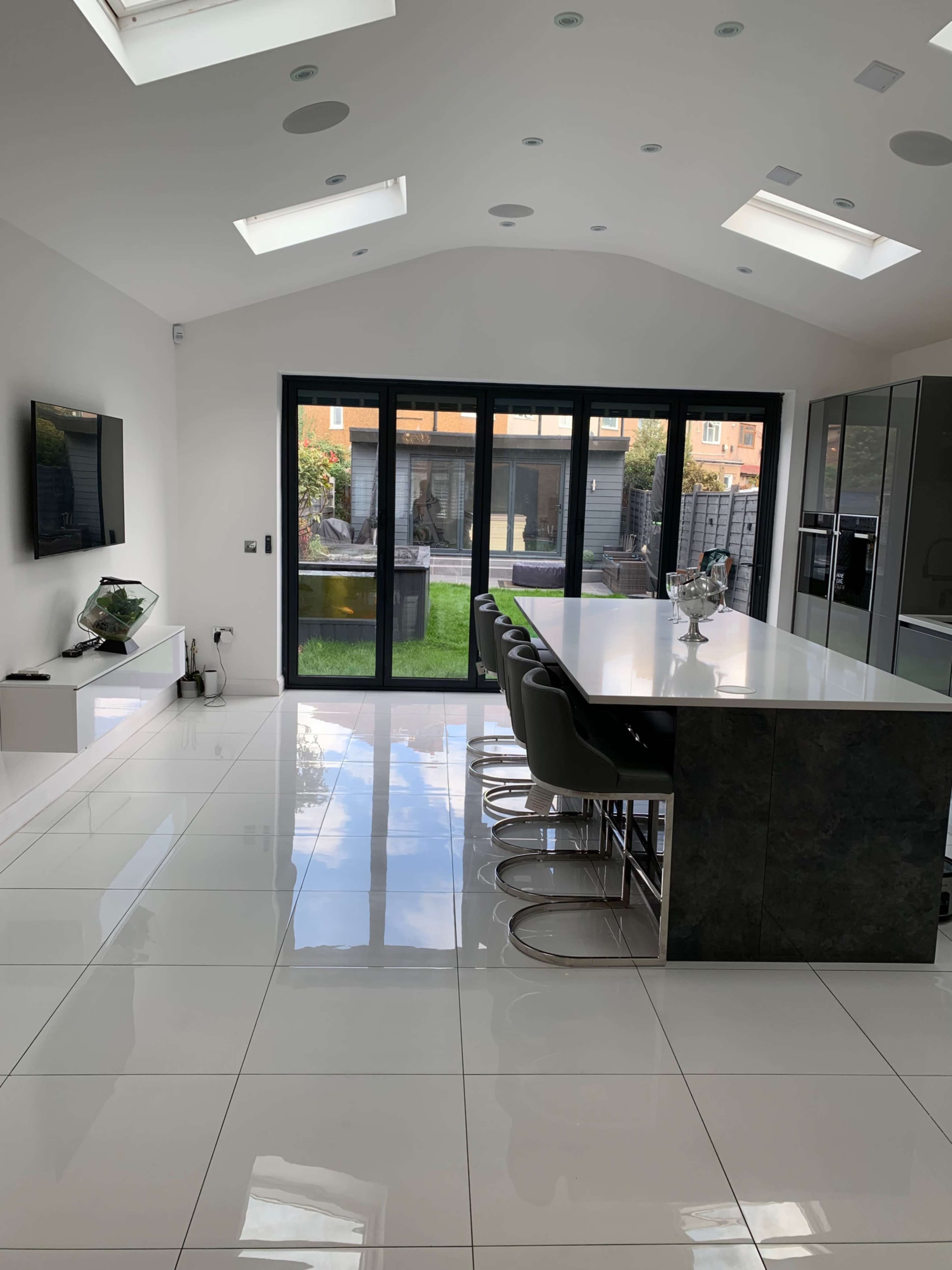 A modern kitchen with a large island bar, sleek cabinetry, and floor-to-ceiling glass doors leading to an outdoor garden.