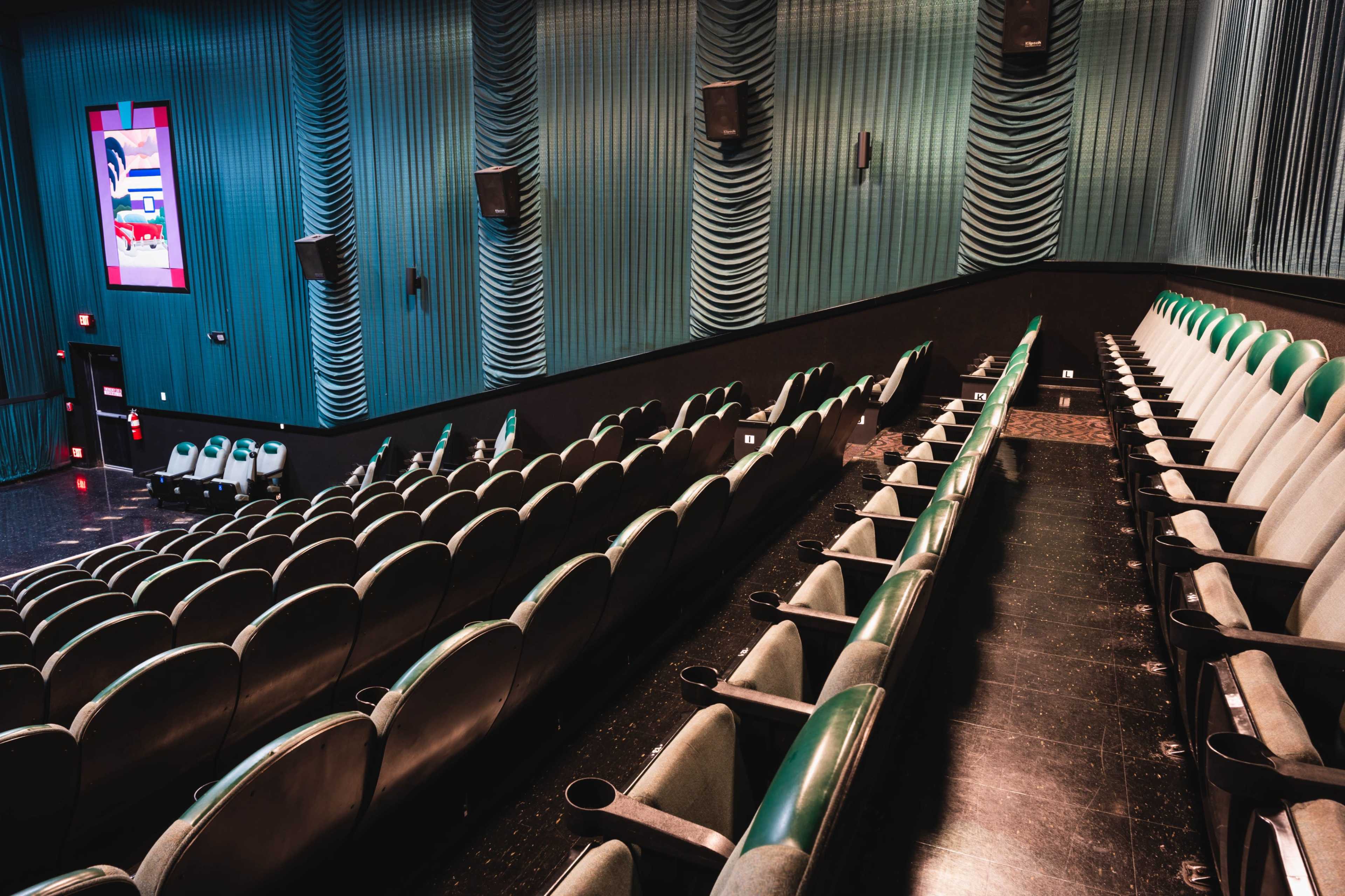 The interior of a theater with green and gray seating arranged in rows and soft blue walls.