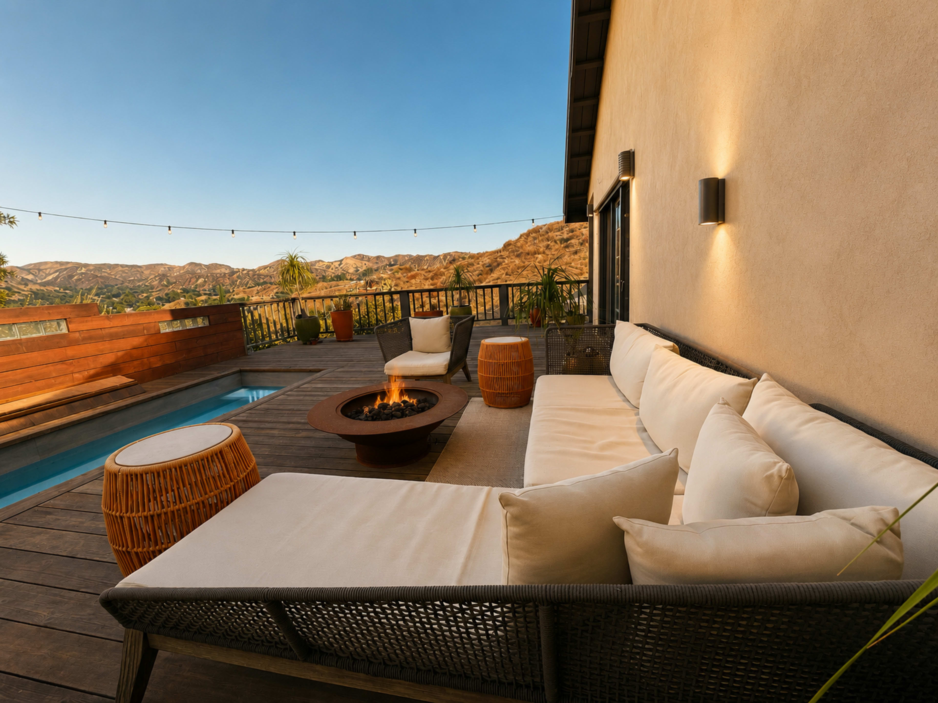 A modern outdoor patio features a comfortable seating area with a fire pit, surrounded by a pool and overlooking a mountainous landscape.