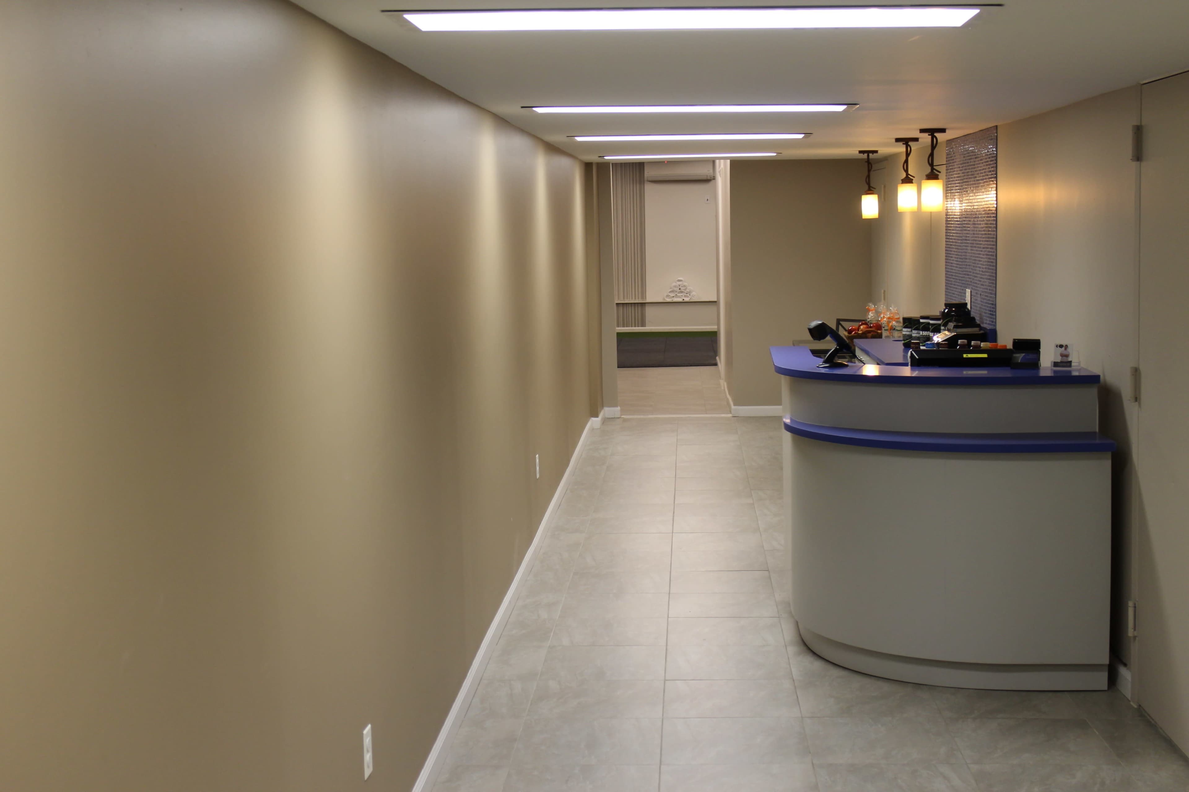 The image shows a modern reception area with a curved front desk and a long, well-lit hallway leading to an open space.