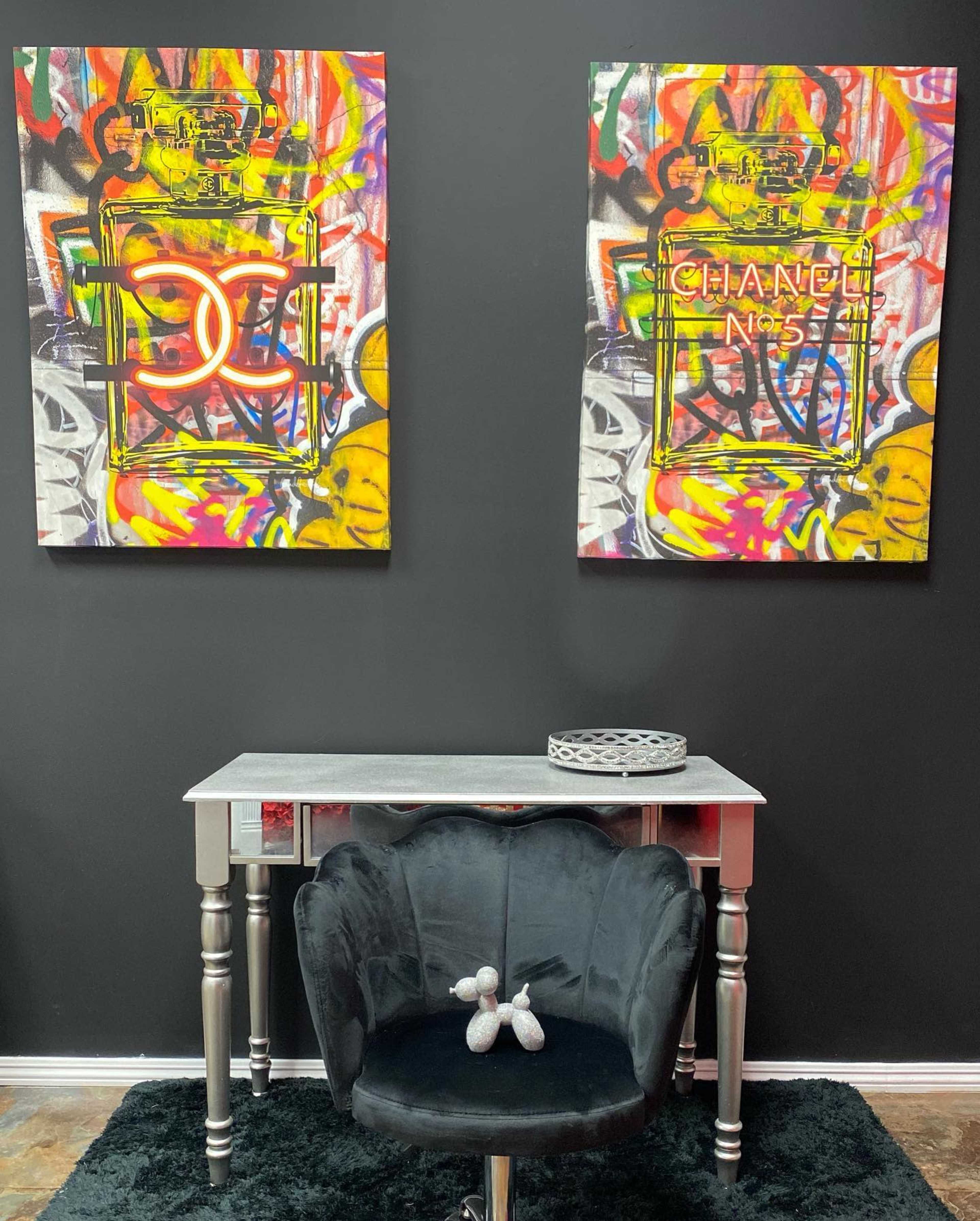 A dark wall adorned with two vibrant, graffiti-style paintings, a silver console table, and a black velvet chair with a decorative piece on the table.