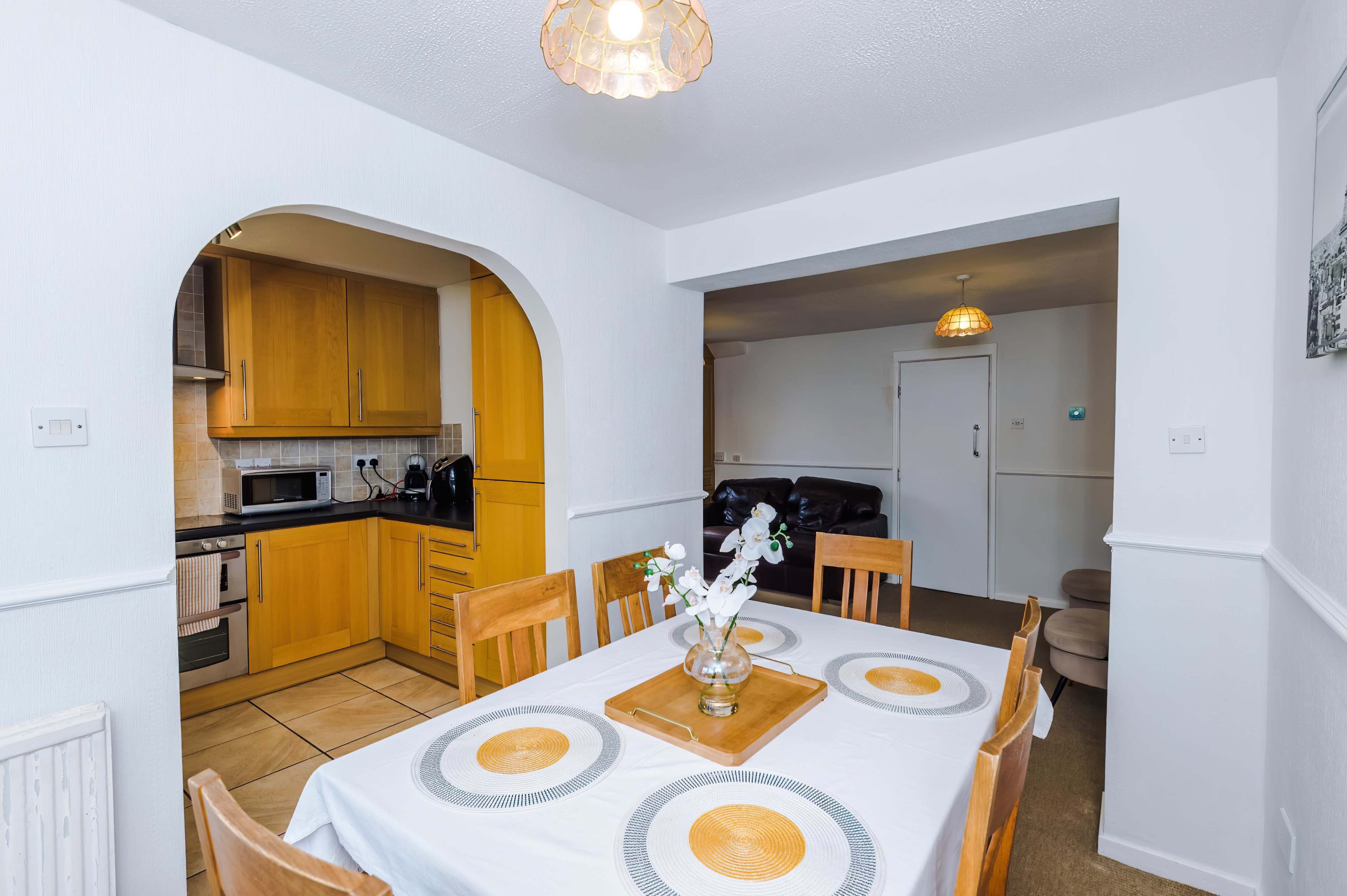 A dining area features a table set with a white tablecloth and golden plates, adjacent to a kitchen with wooden cabinetry and stainless steel appliances.