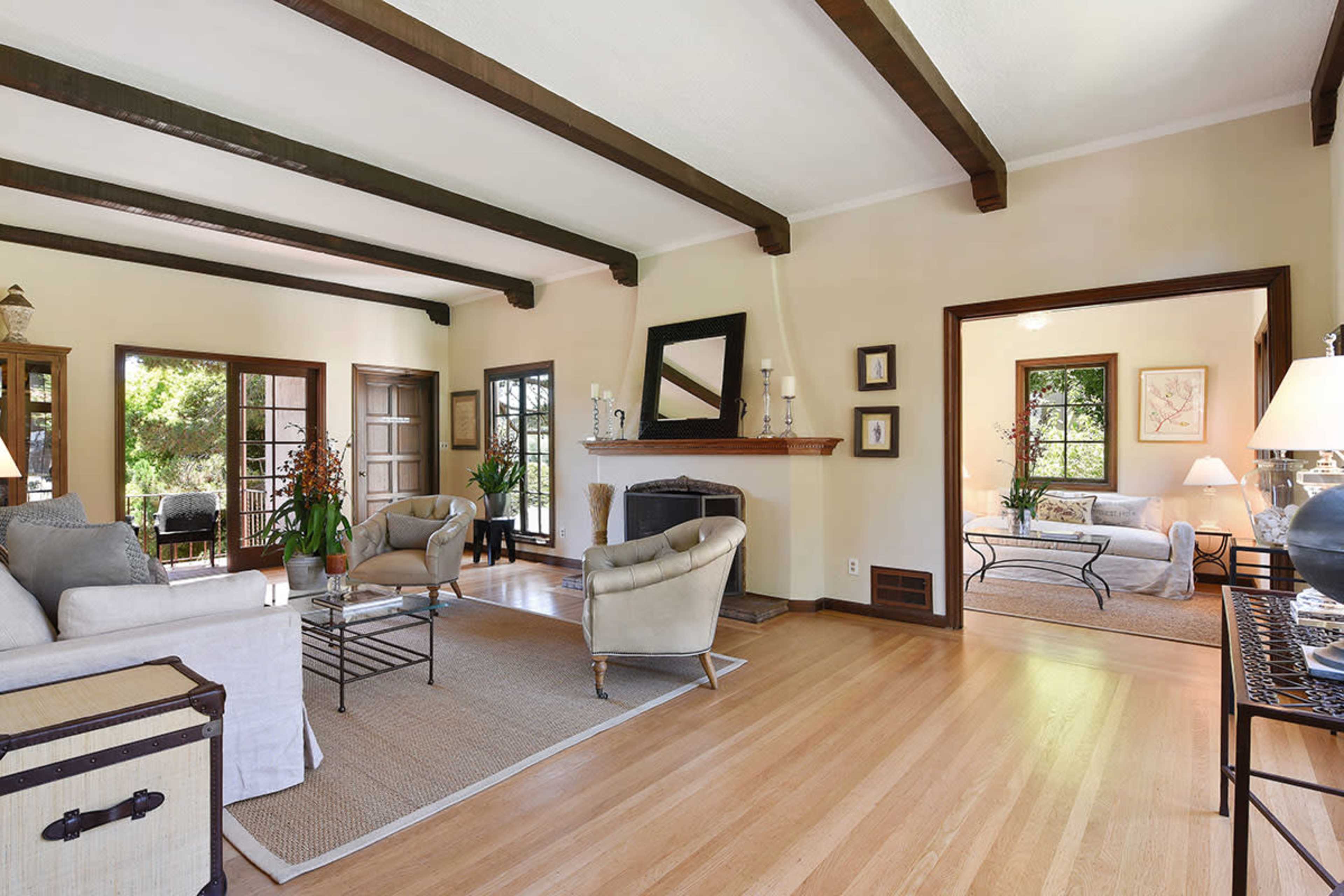 A well-lit living room features a fireplace, hardwood floors, and large windows, with seating arranged around a central coffee table.