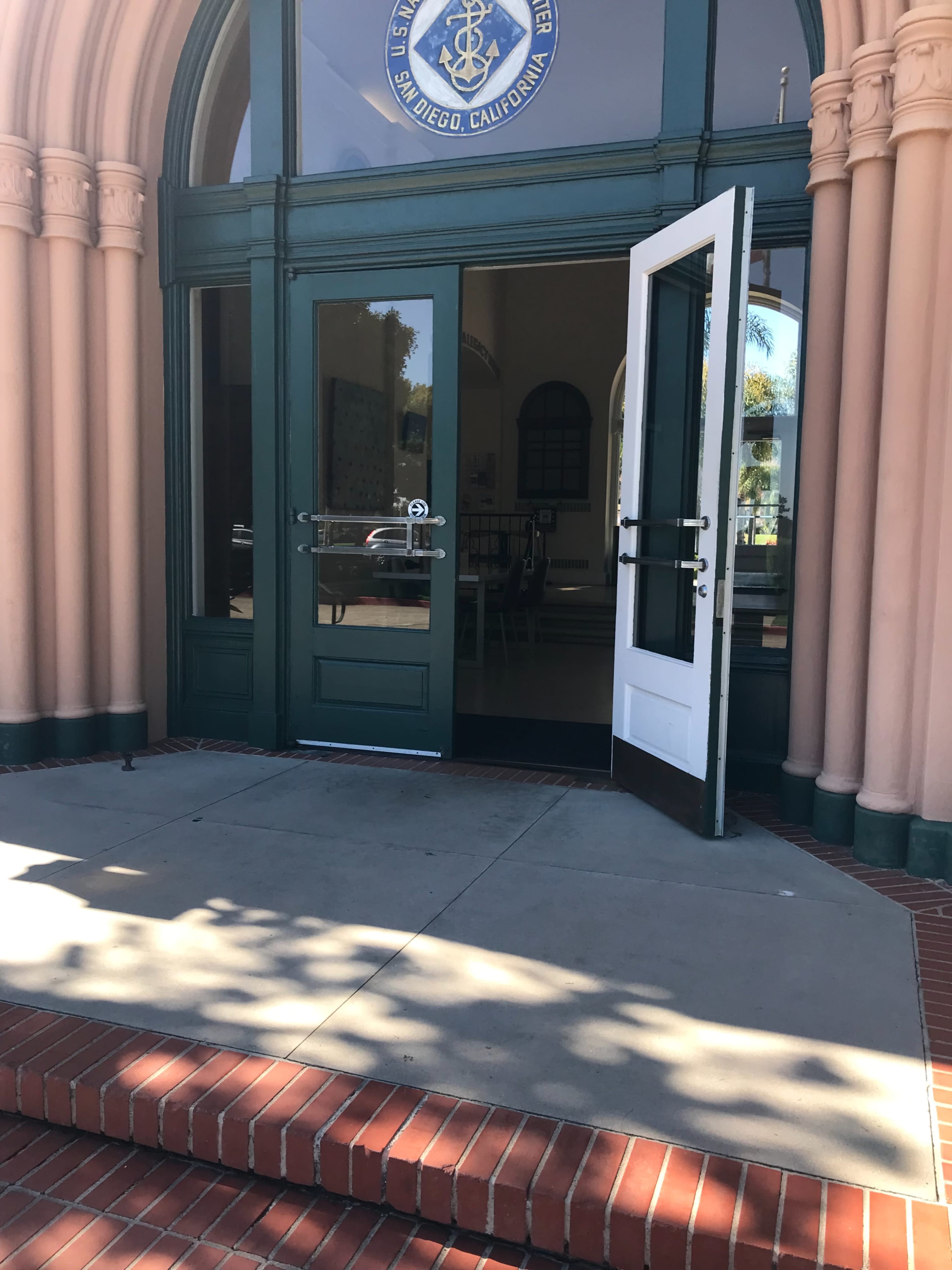The entrance of a building with an open door, revealing a glimpse of the interior and a seal on the wall above.
