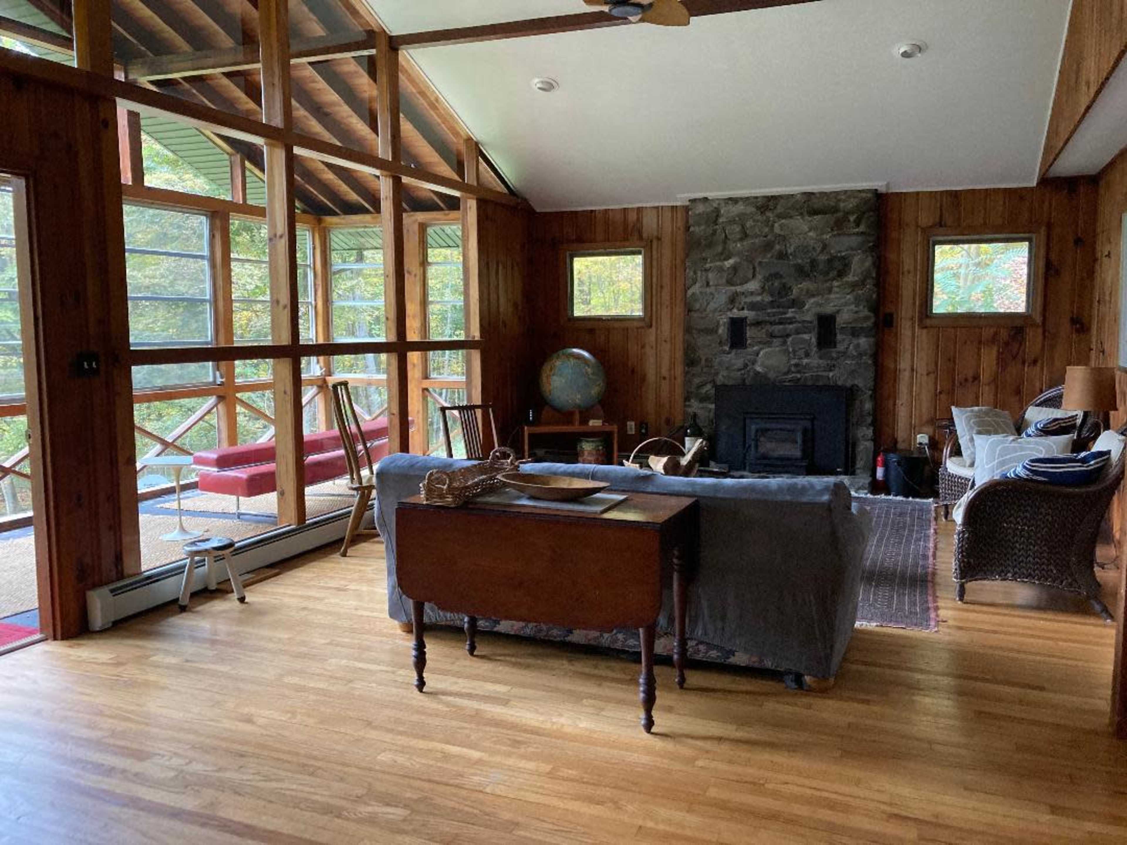 A wooden-paneled living room with a stone fireplace, a globe on a side table, and large windows letting in natural light.