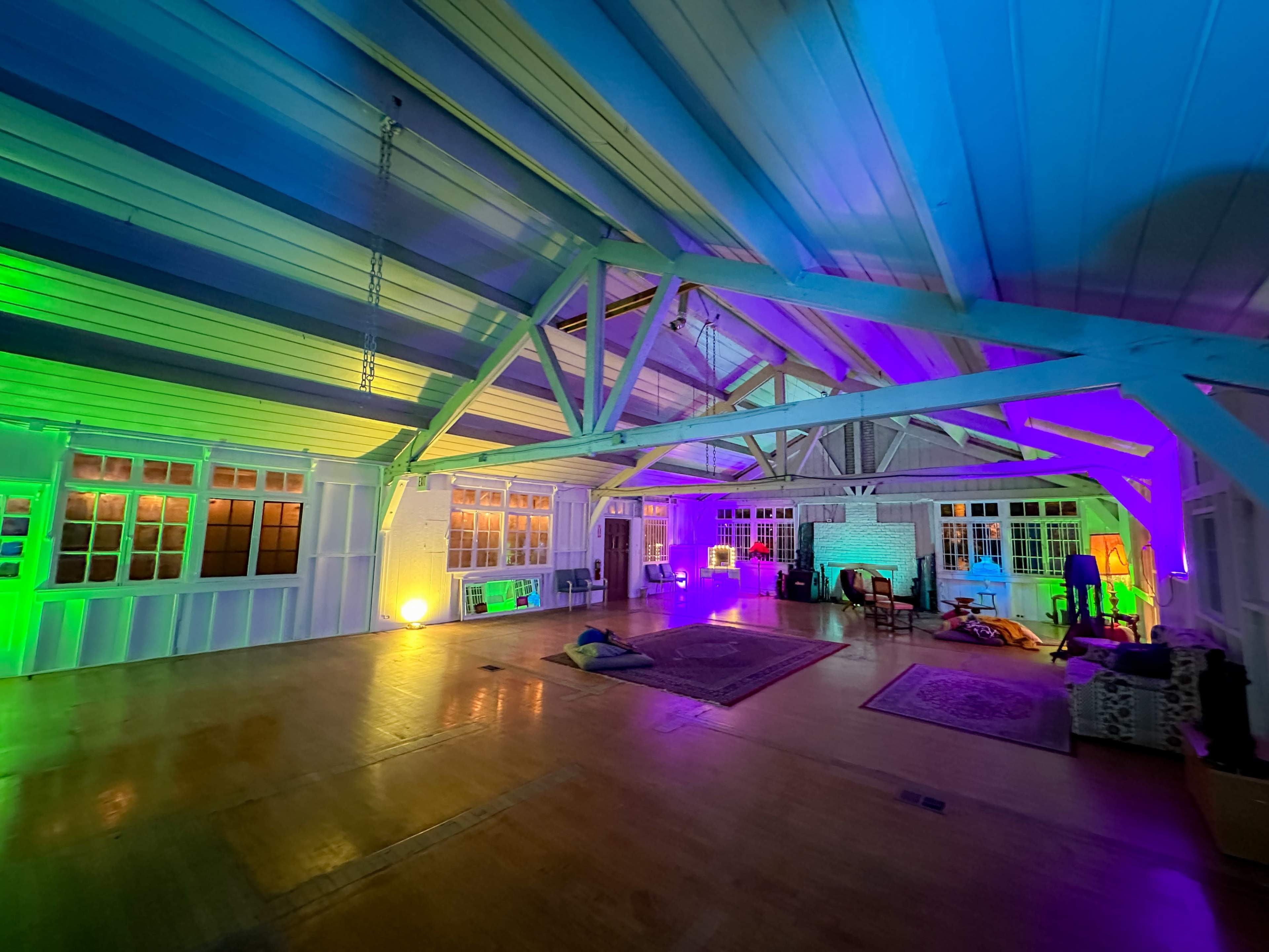 The image shows a spacious interior room with wooden beams, illuminated by colorful lighting in green and purple tones.