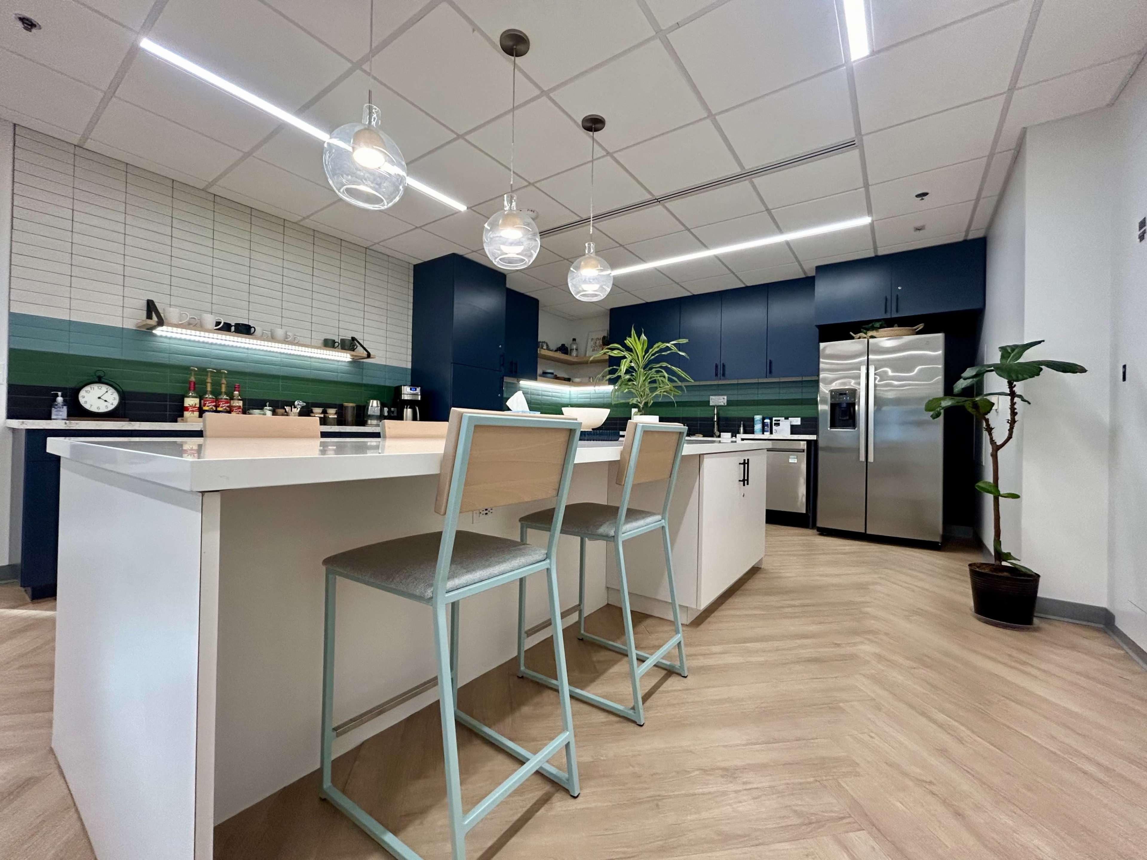 The image shows a modern kitchen with blue cabinetry, a central island with bar stools, and pendant lighting above.