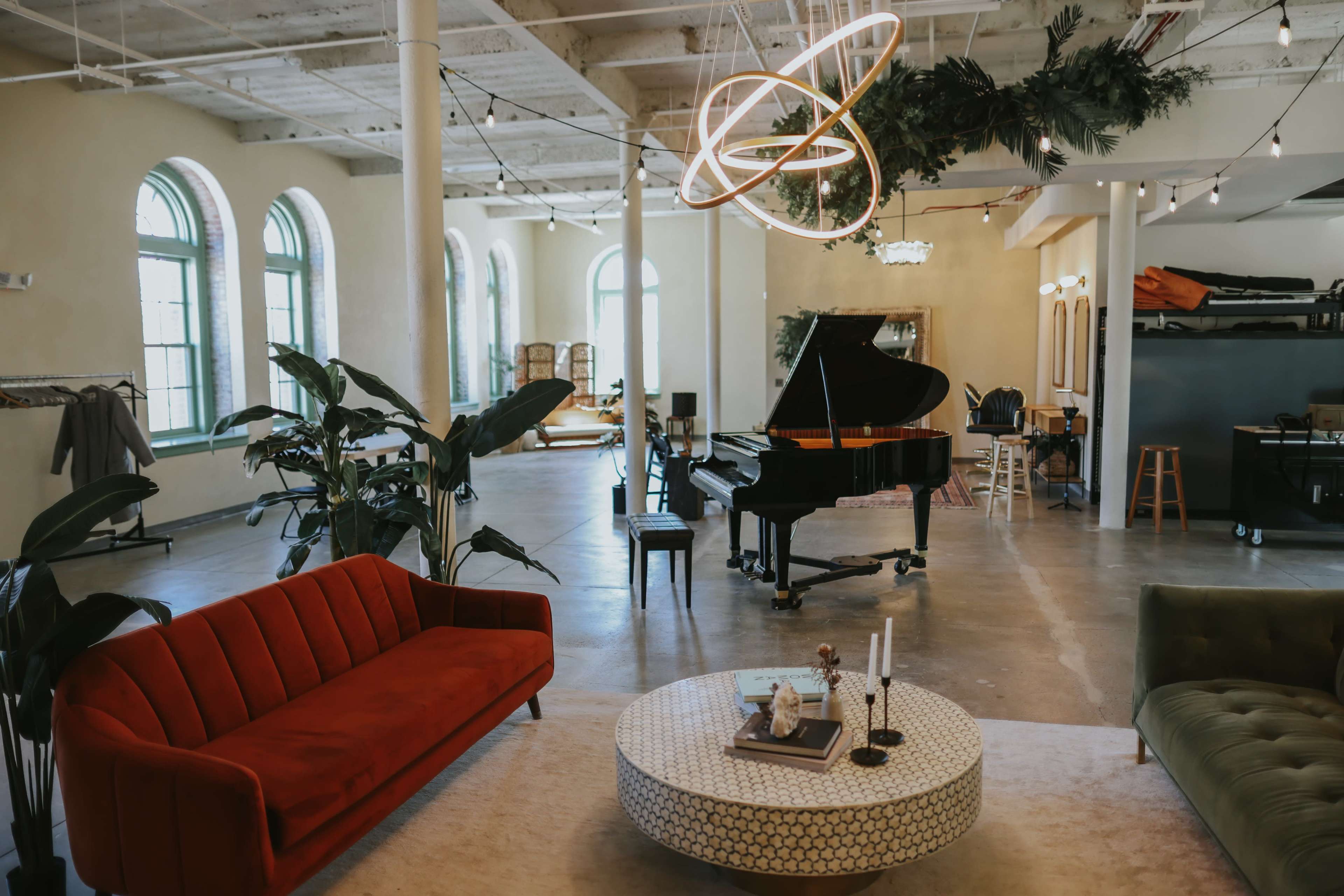 The image depicts a spacious, modern living area featuring a grand piano, a red sofa, and a round coffee table with candles.