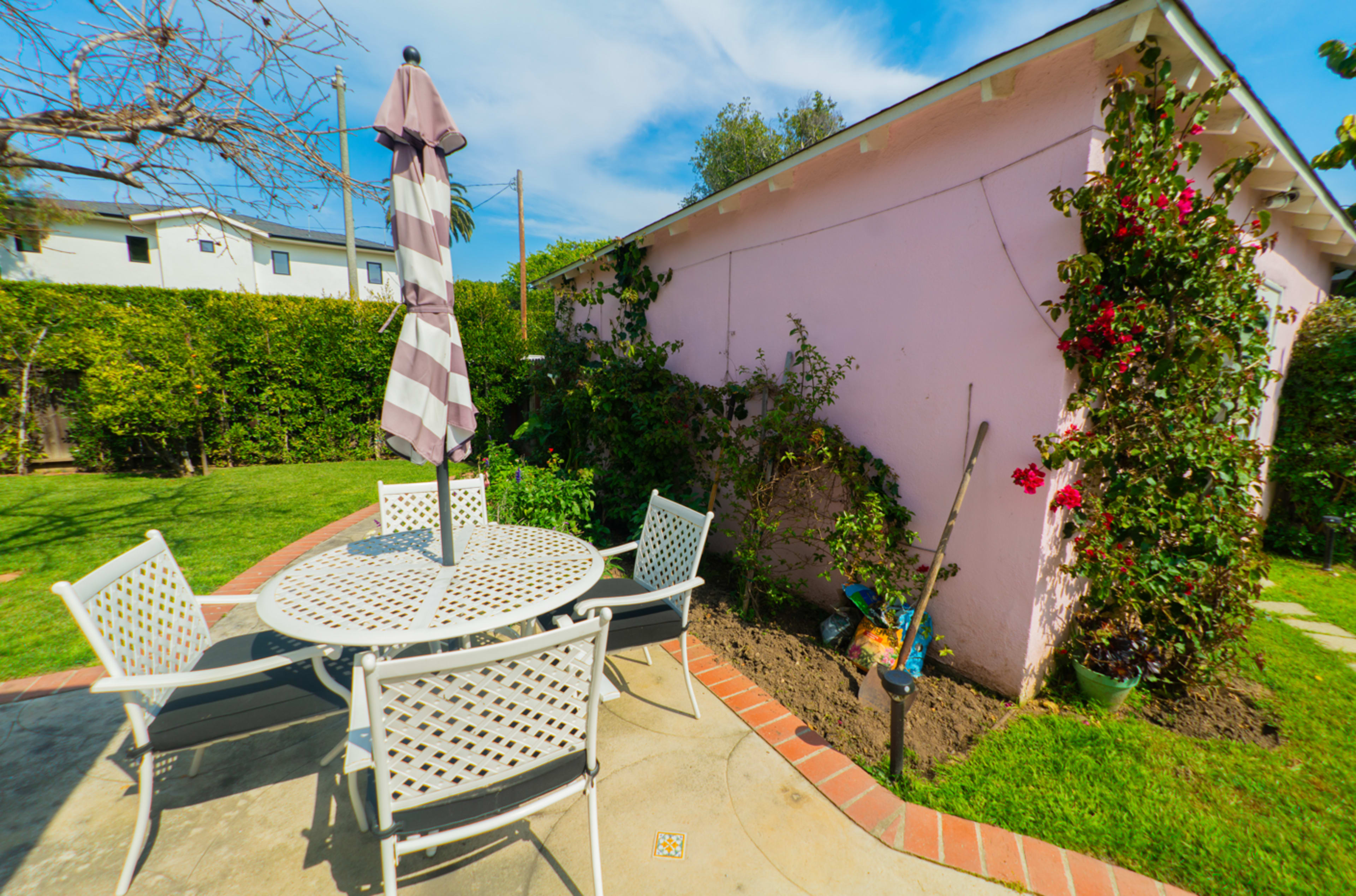 A patio area with a round table and chairs is set up in front of a pink wall covered in green vines.