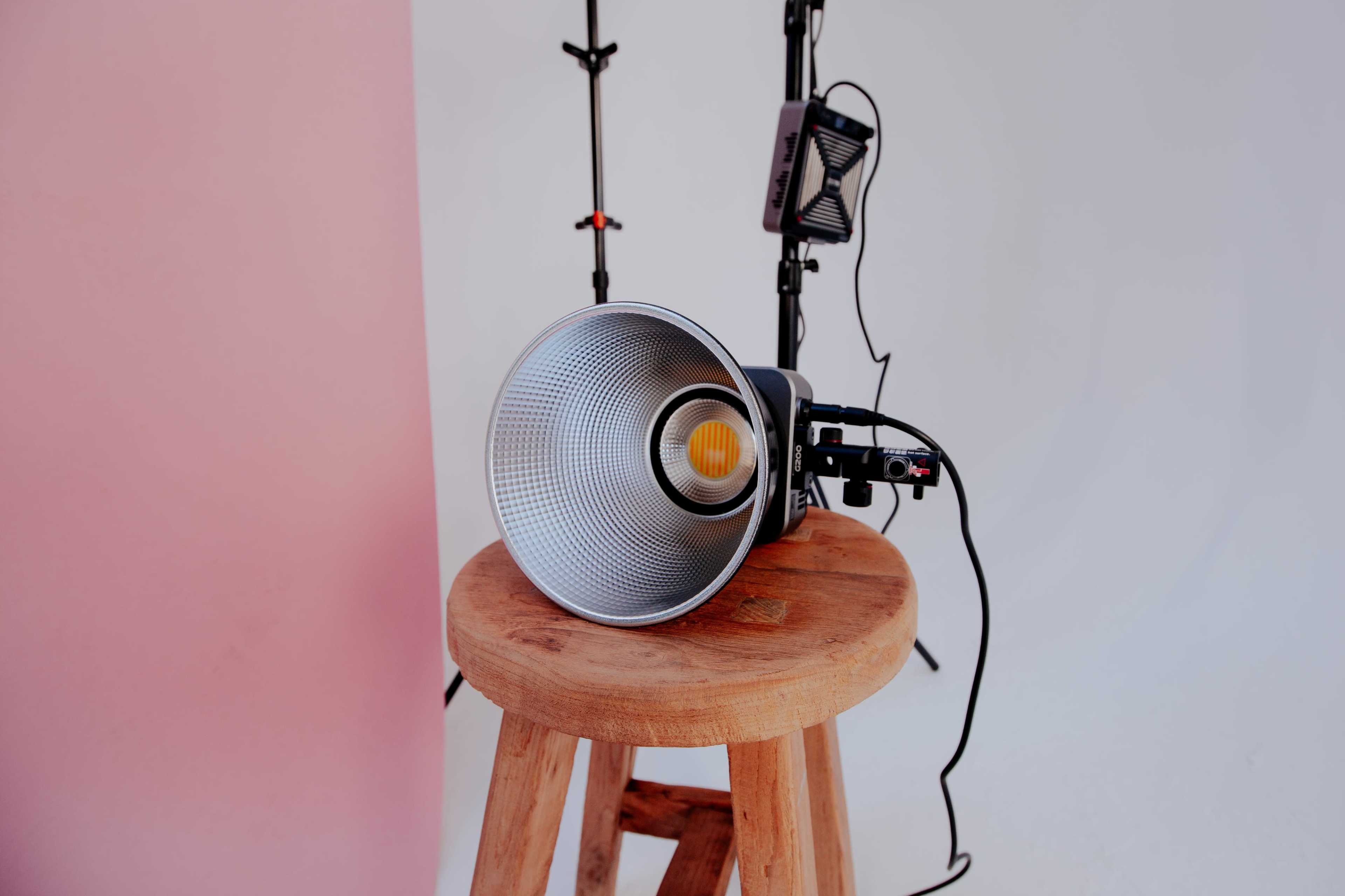 A spotlight is positioned on a wooden stool against a backdrop of pink and white walls.