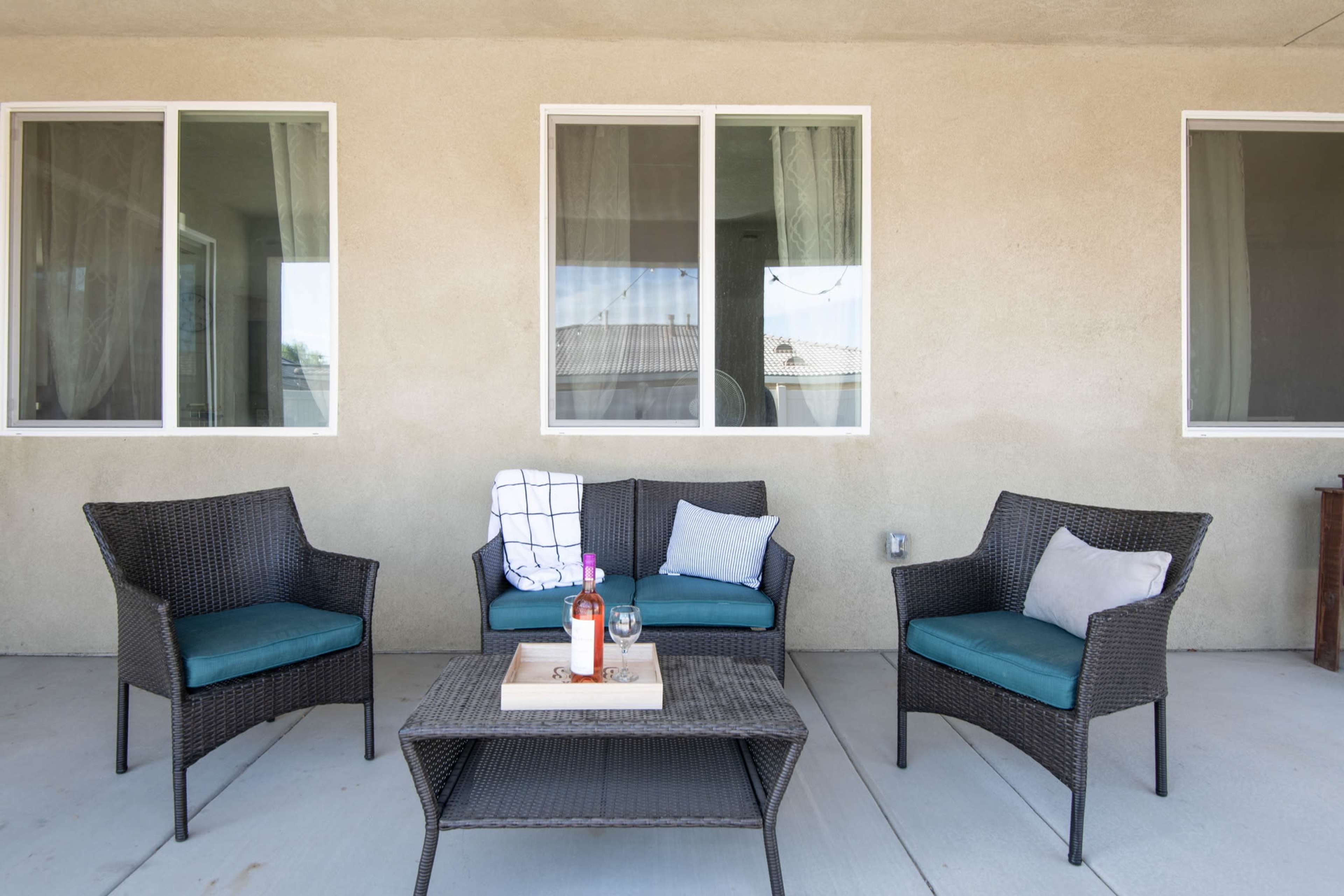 A set of wicker patio furniture, including two armchairs and a couch, is arranged around a coffee table on a concrete patio.