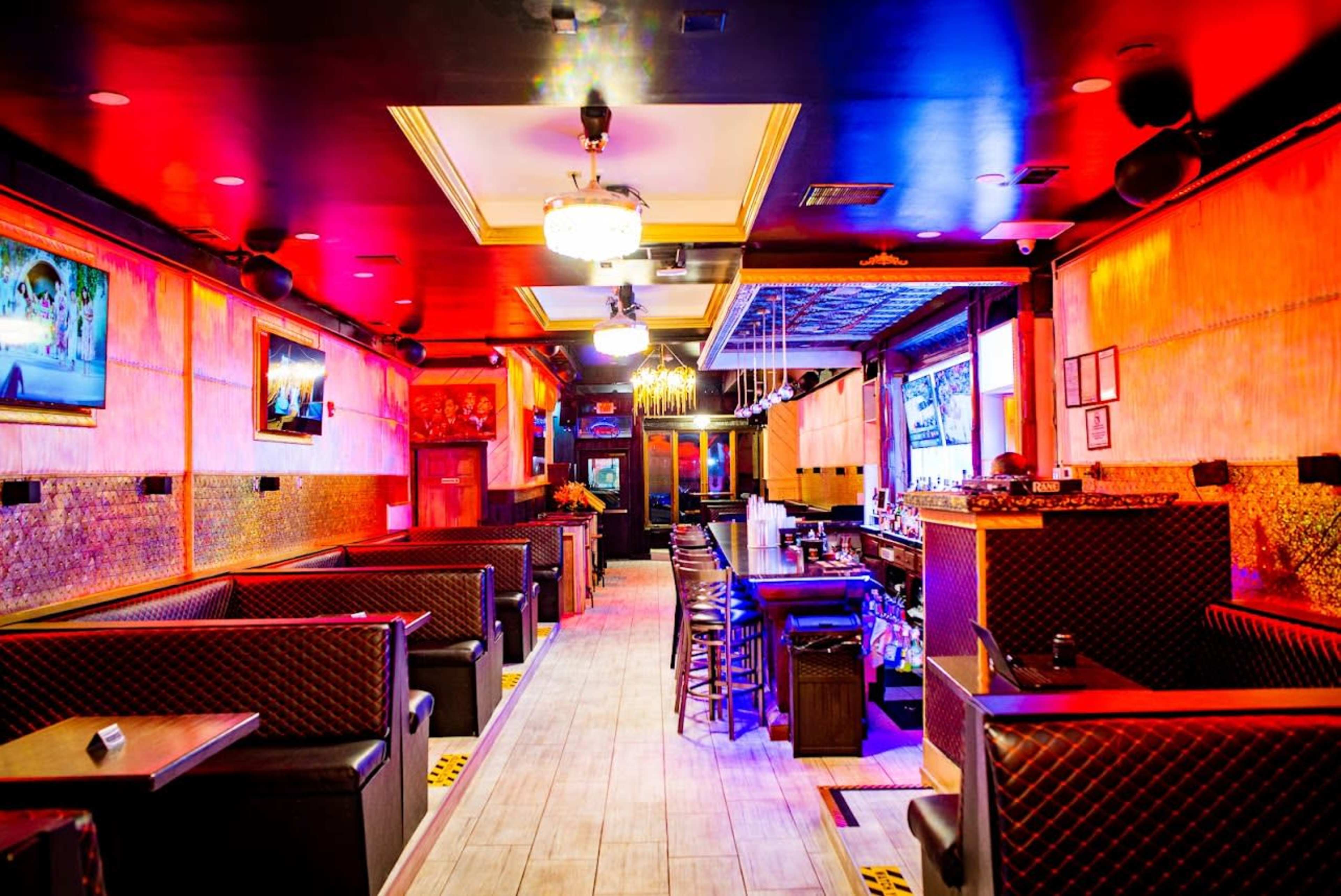 The interior of a restaurant features booths on either side of a central aisle, with colorful lighting and decorative walls.