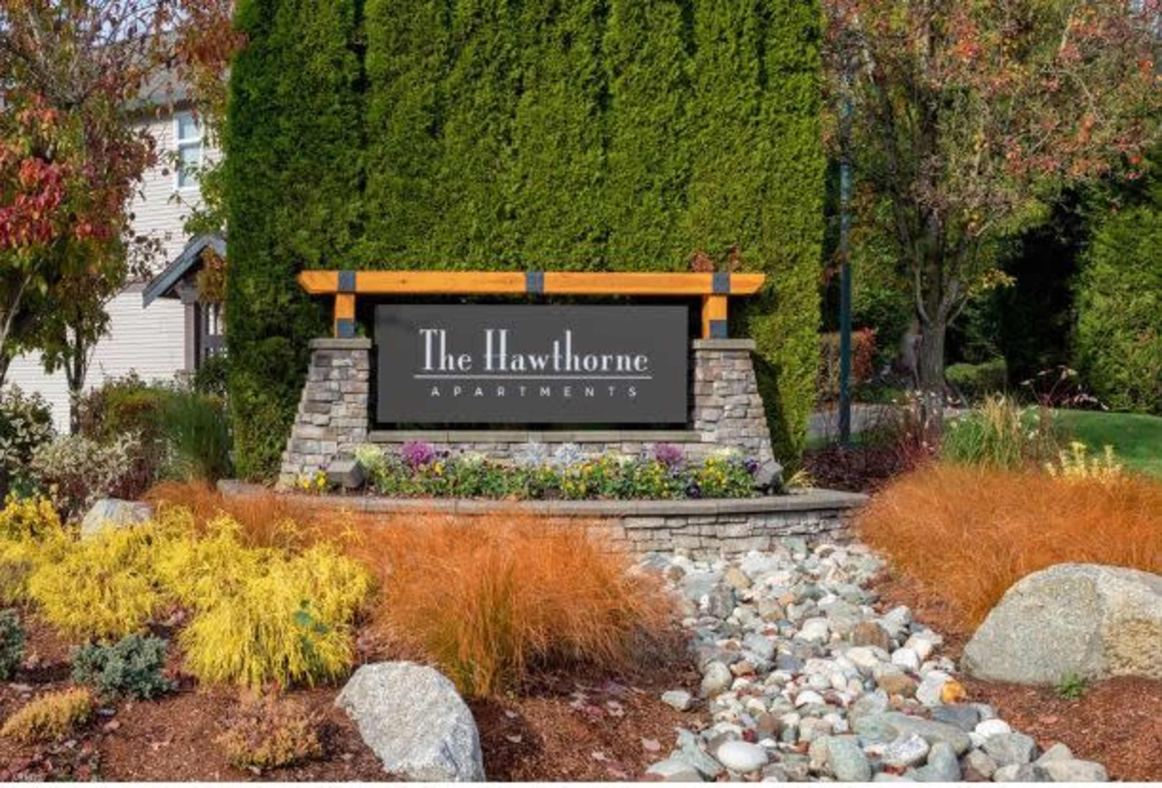 The image shows a sign for "The Hawthorne Apartments" surrounded by landscaped foliage and decorative stone features.