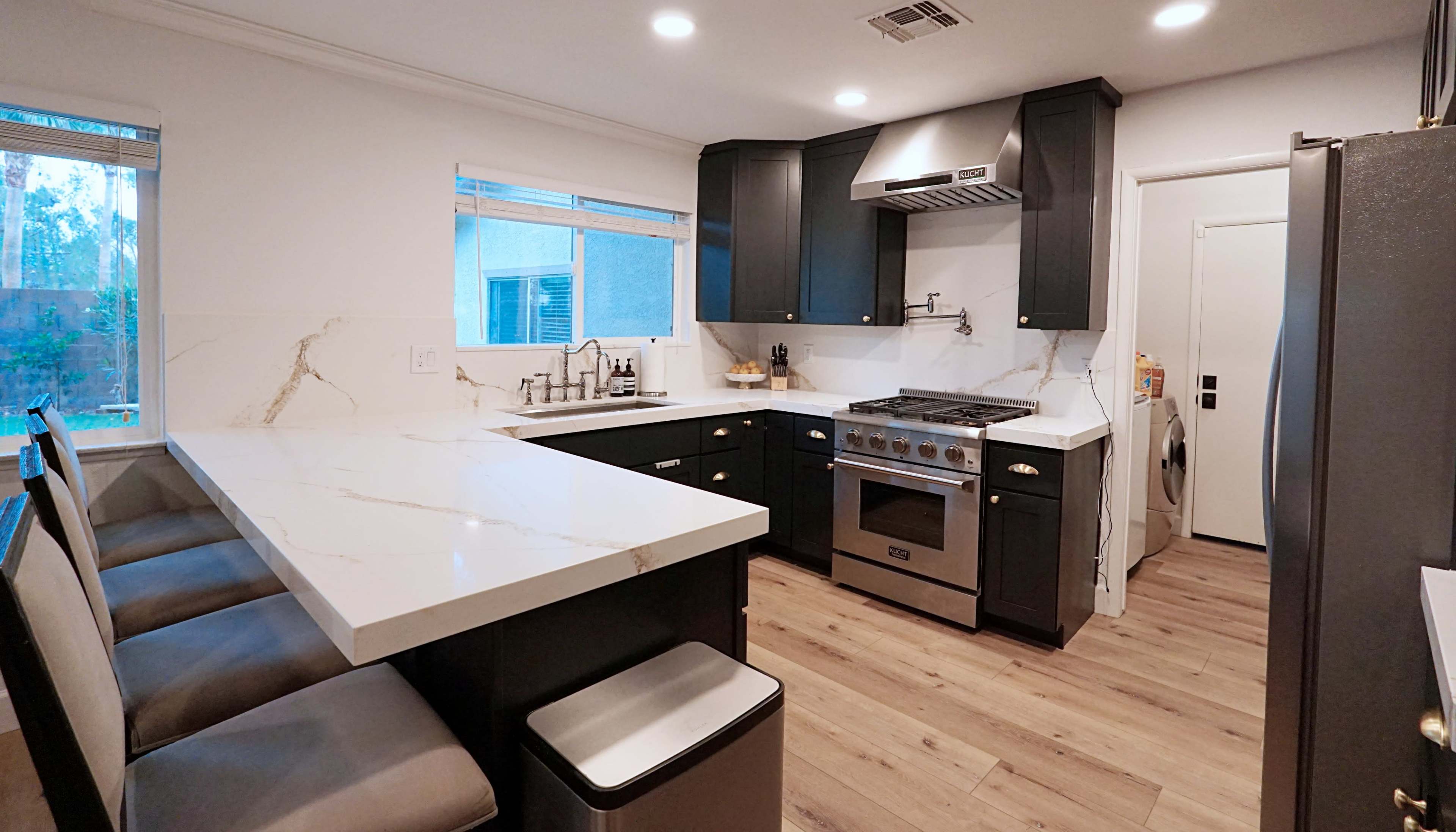 The kitchen features dark cabinets, a marble countertop, and stainless steel appliances with a large island and seating.