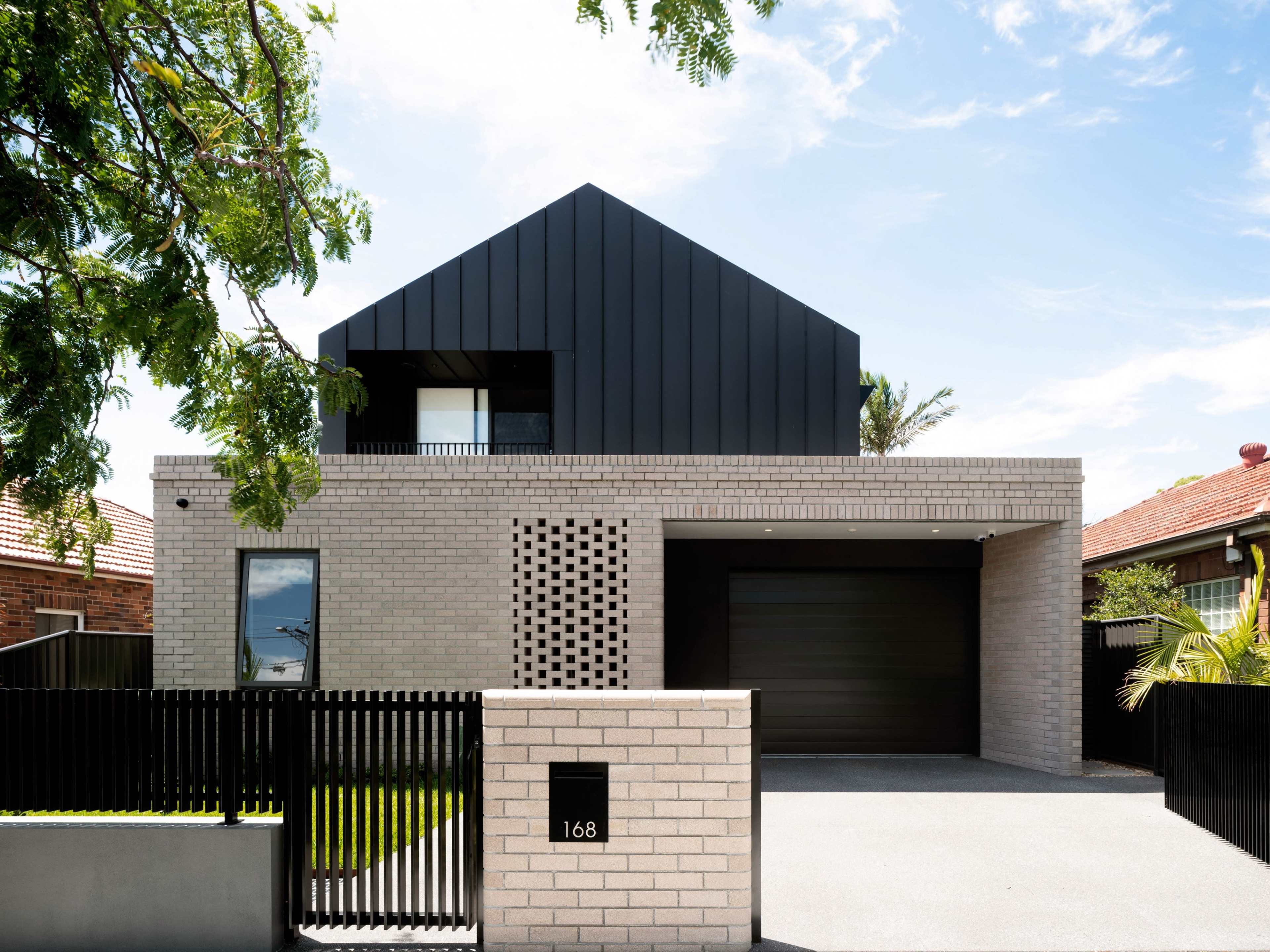 A modern two-story house with a combination of brick and black metal siding, featuring a driveway and a decorative fence.